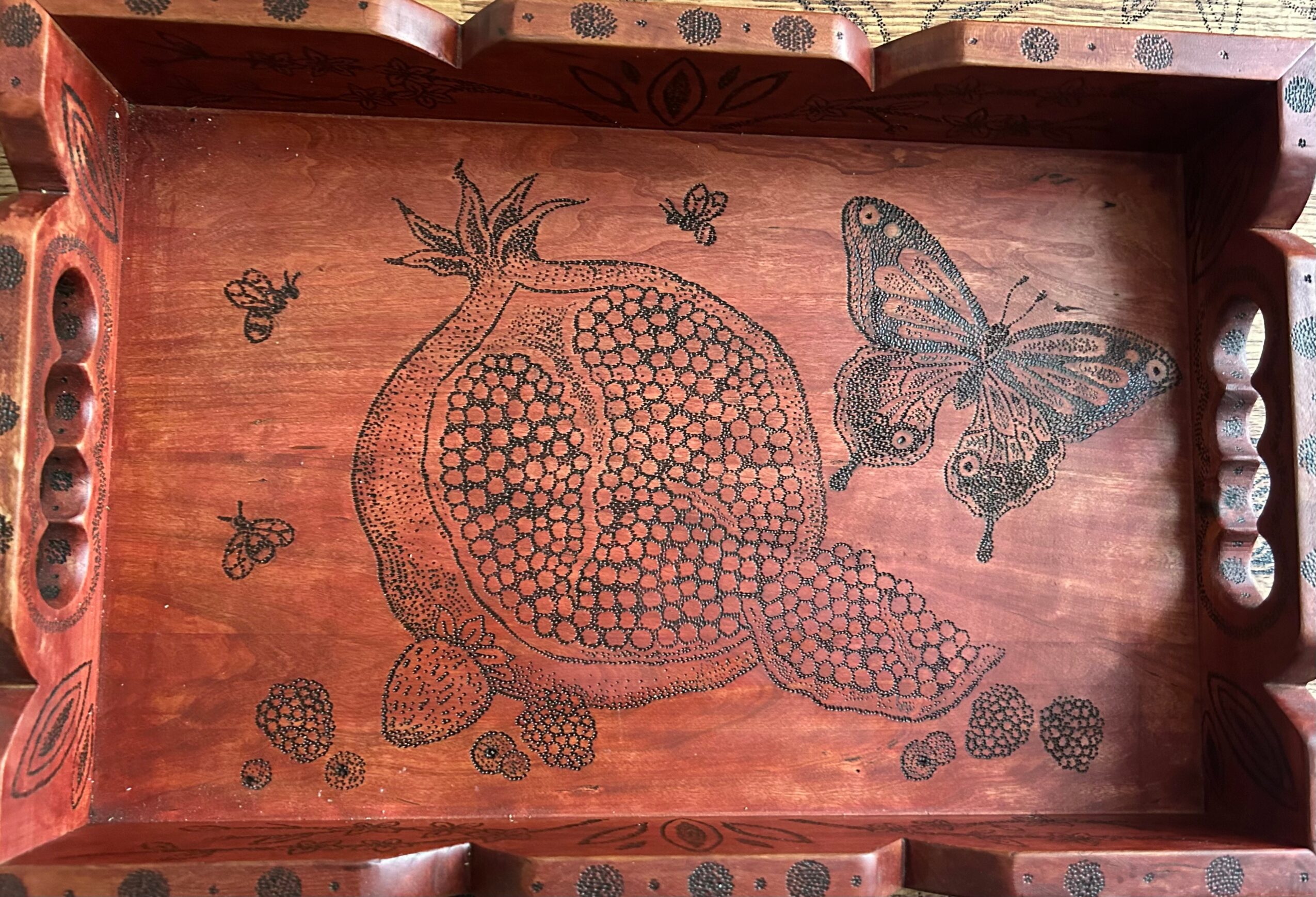 Wooden tray with engraved pomegranate, butterfly, and bees, featuring detailed line art and decorative borders.
