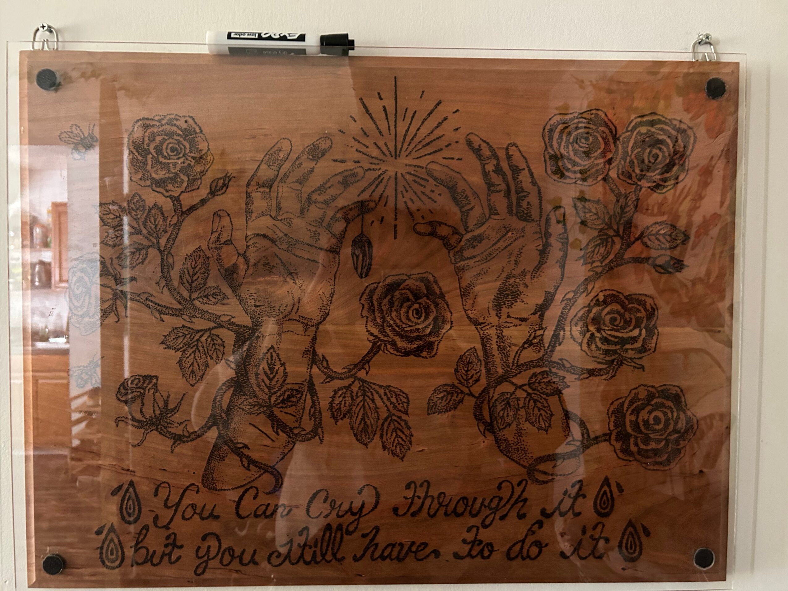 Decorative wooden board with floral and hand illustrations, featuring roses, hands, and a central burst design, with text and teardrop symbols.