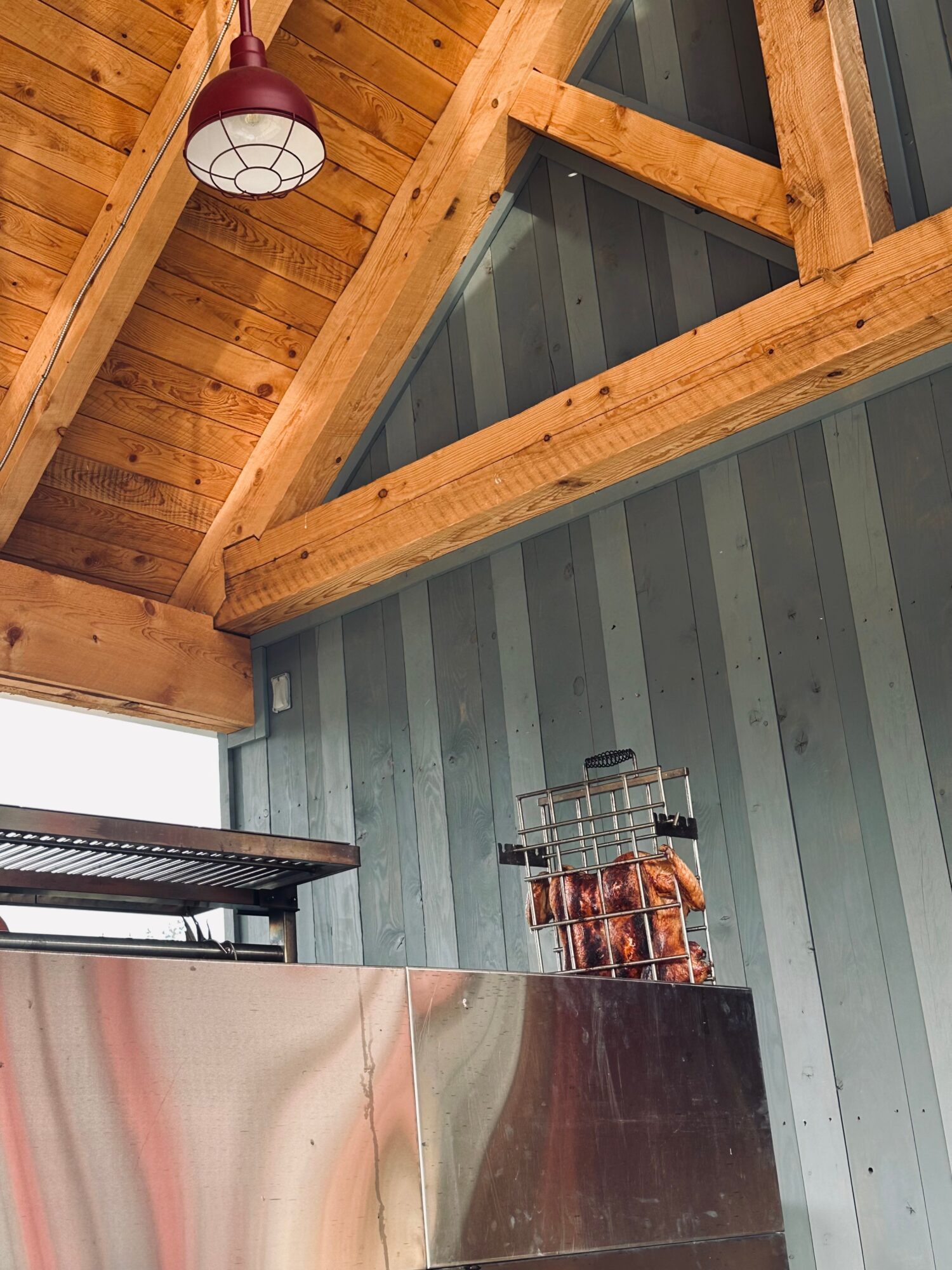 Interior view showing wooden beams, a hanging purple lamp, and a metal counter with a glass container of cookies.