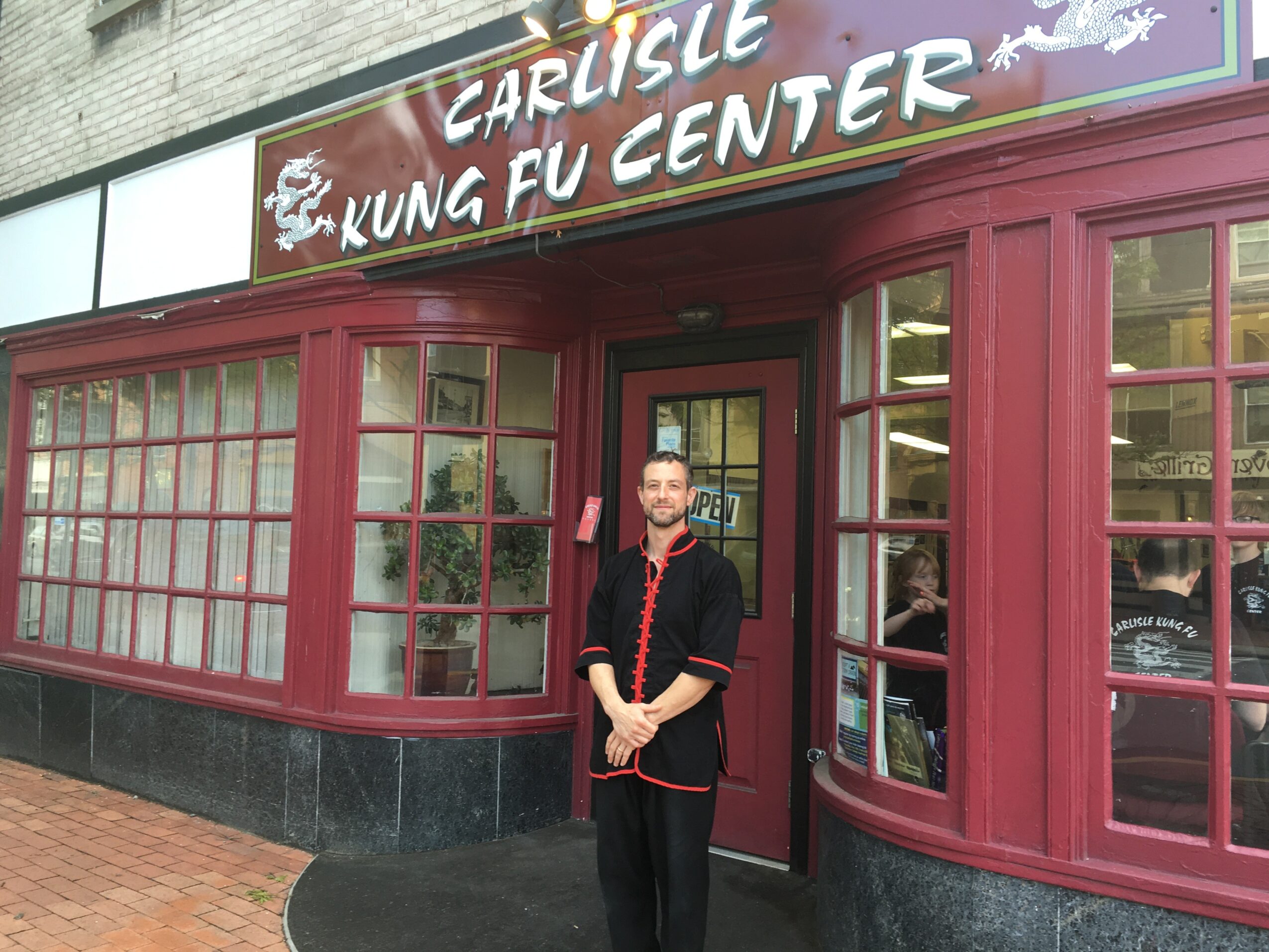 Person standing outside a martial arts center with a sign reading 'Carlisle Kung Fu Center' above the entrance.
