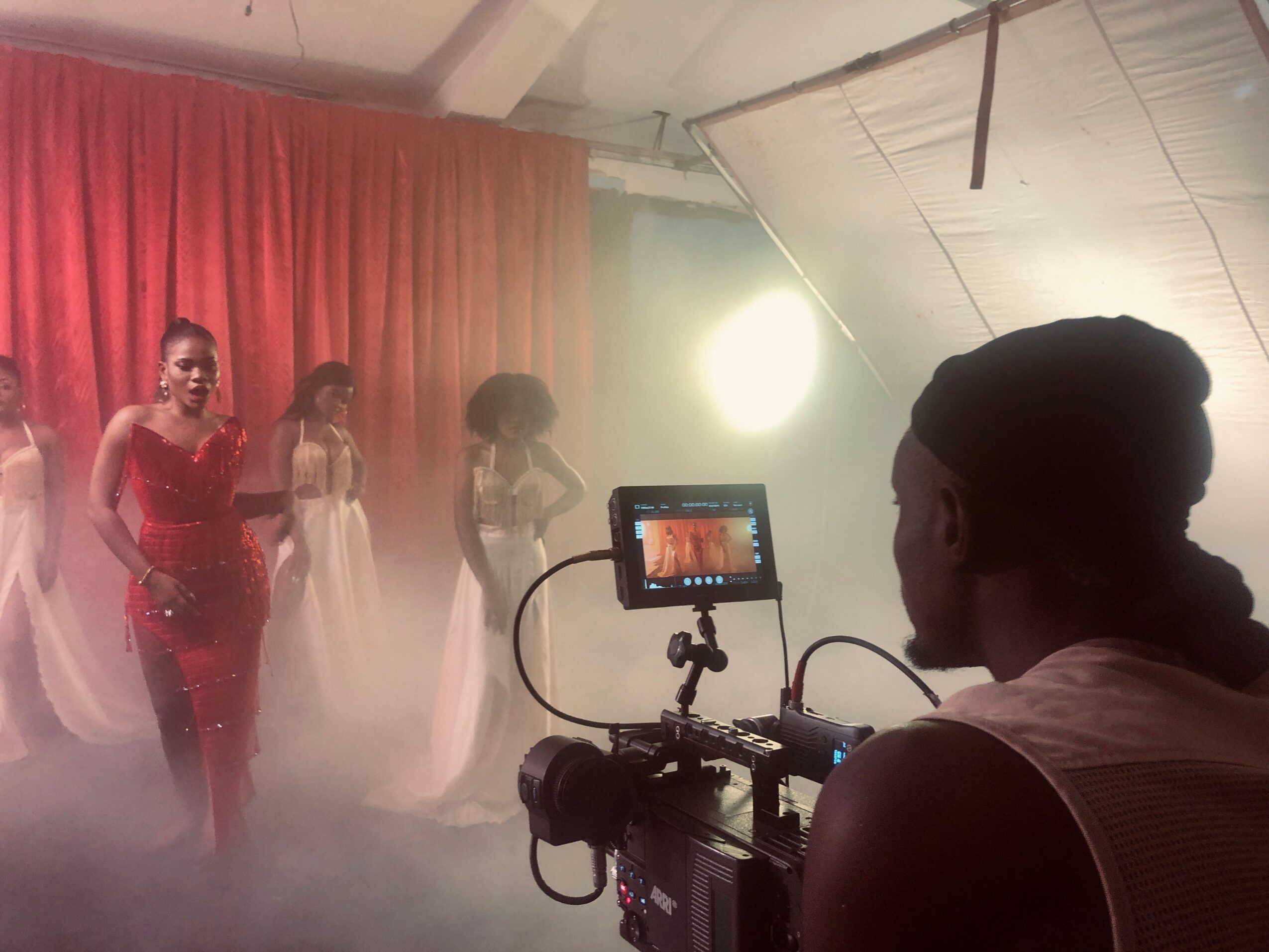 Person filming a dance performance with four dancers on stage, red curtain backdrop, and stage lighting.