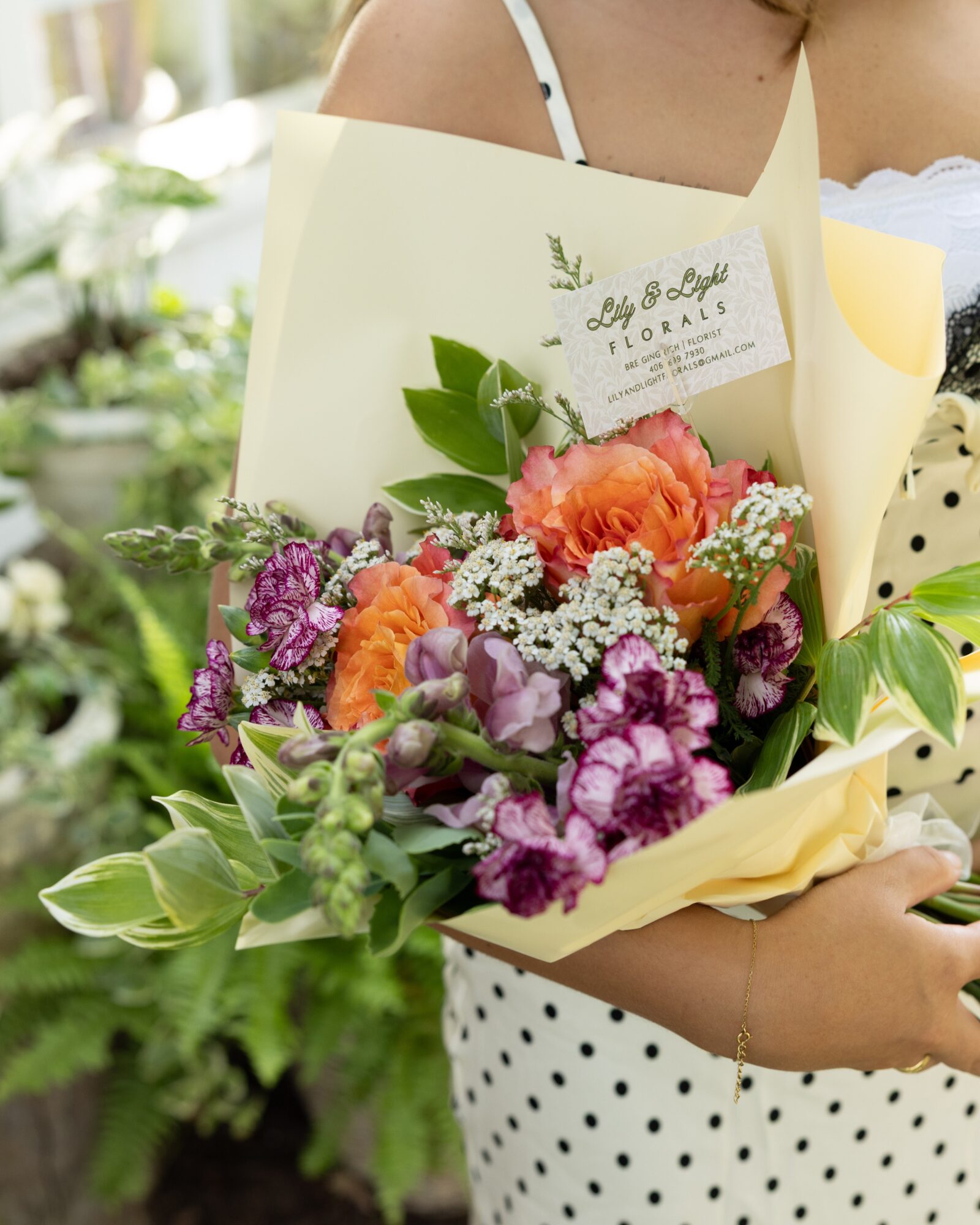 Person holding a colorful bouquet of flowers wrapped in yellow paper, with a label reading 