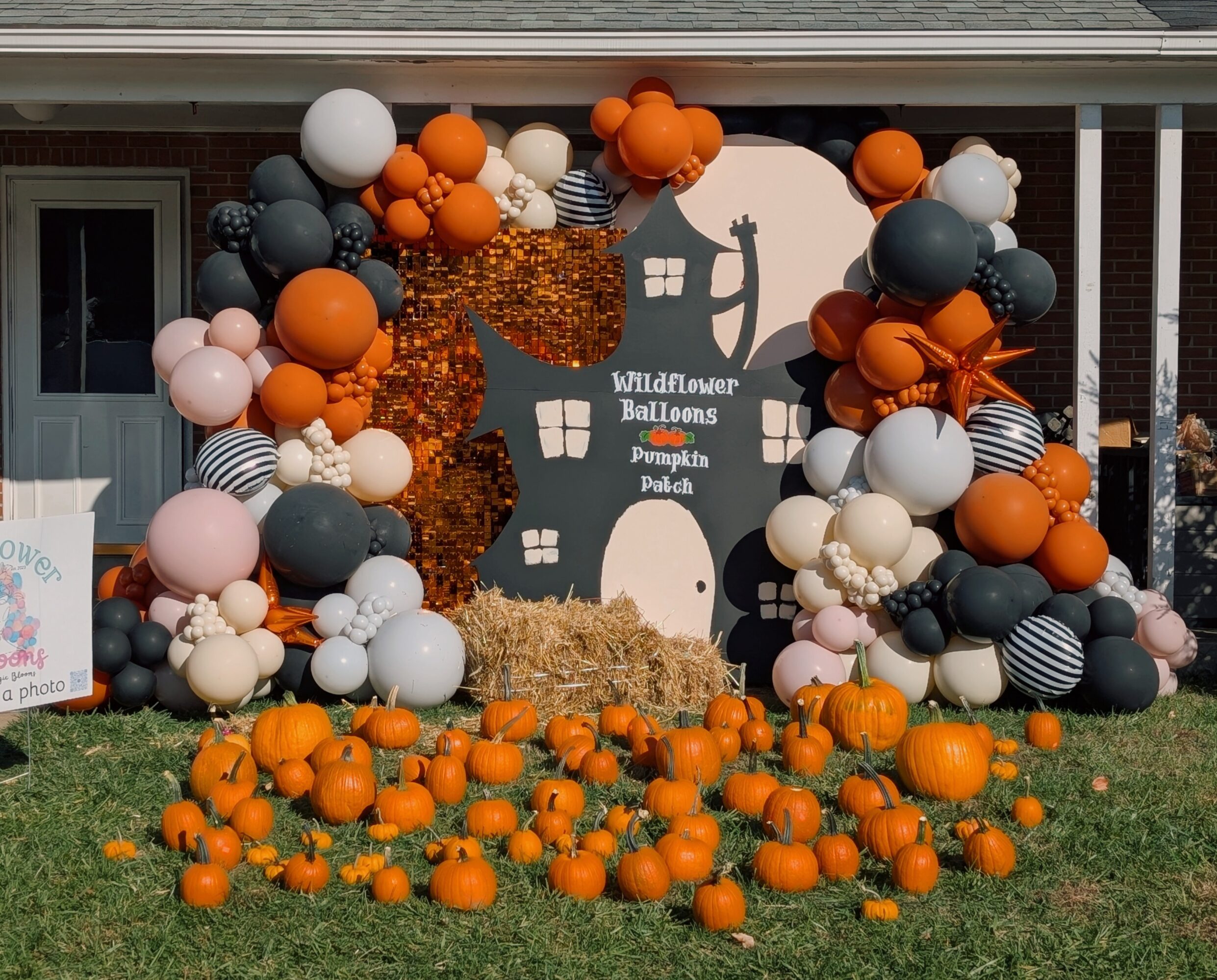 Decorative display with balloons, pumpkins, and a silhouette of a witch on a house-shaped backdrop for a Halloween event.