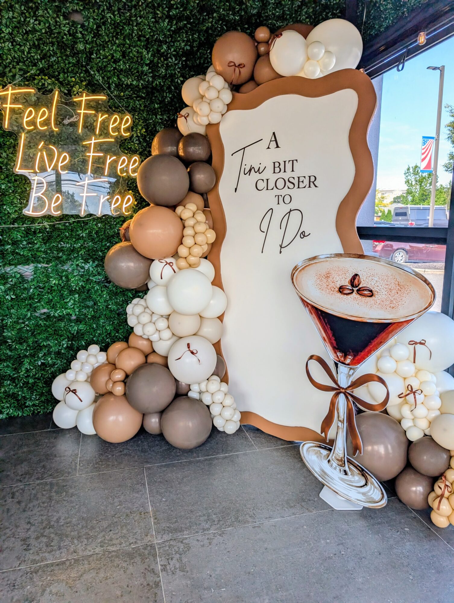 Decorative balloon arrangement with a mirror and a sign, with a neon sign reading 'Feel Free Live Free Be Free' in the background.