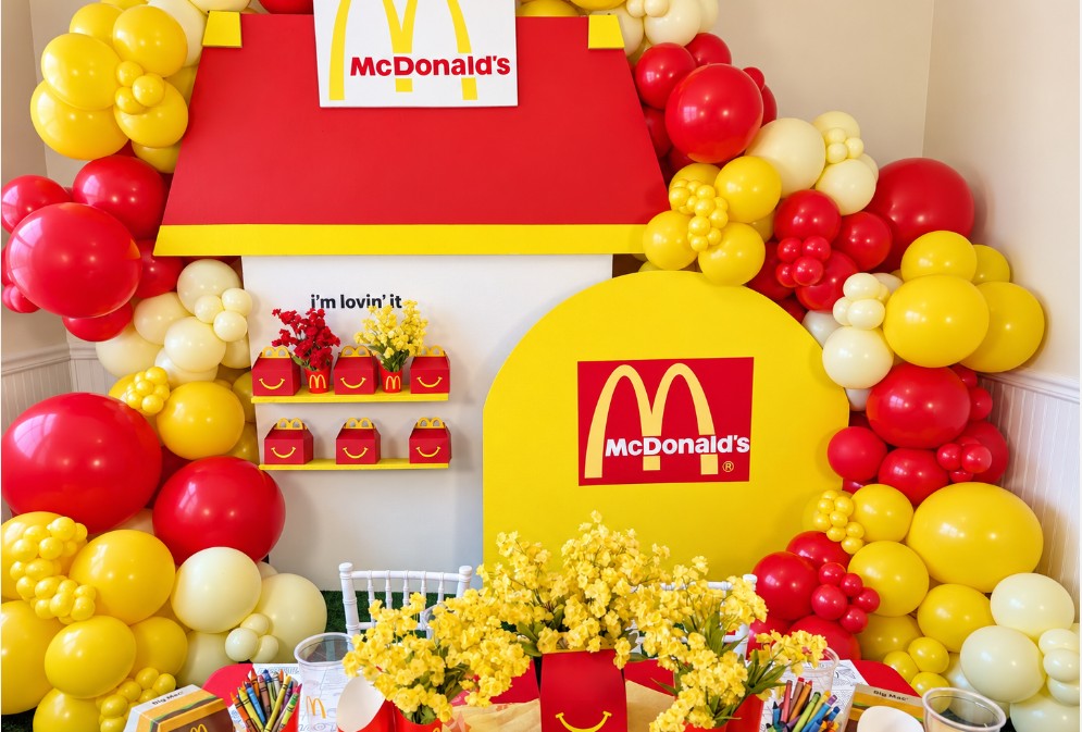 Decorative McDonald's display with balloons, a yellow and red backdrop, and flowers, celebrating the brand's logo and theme.