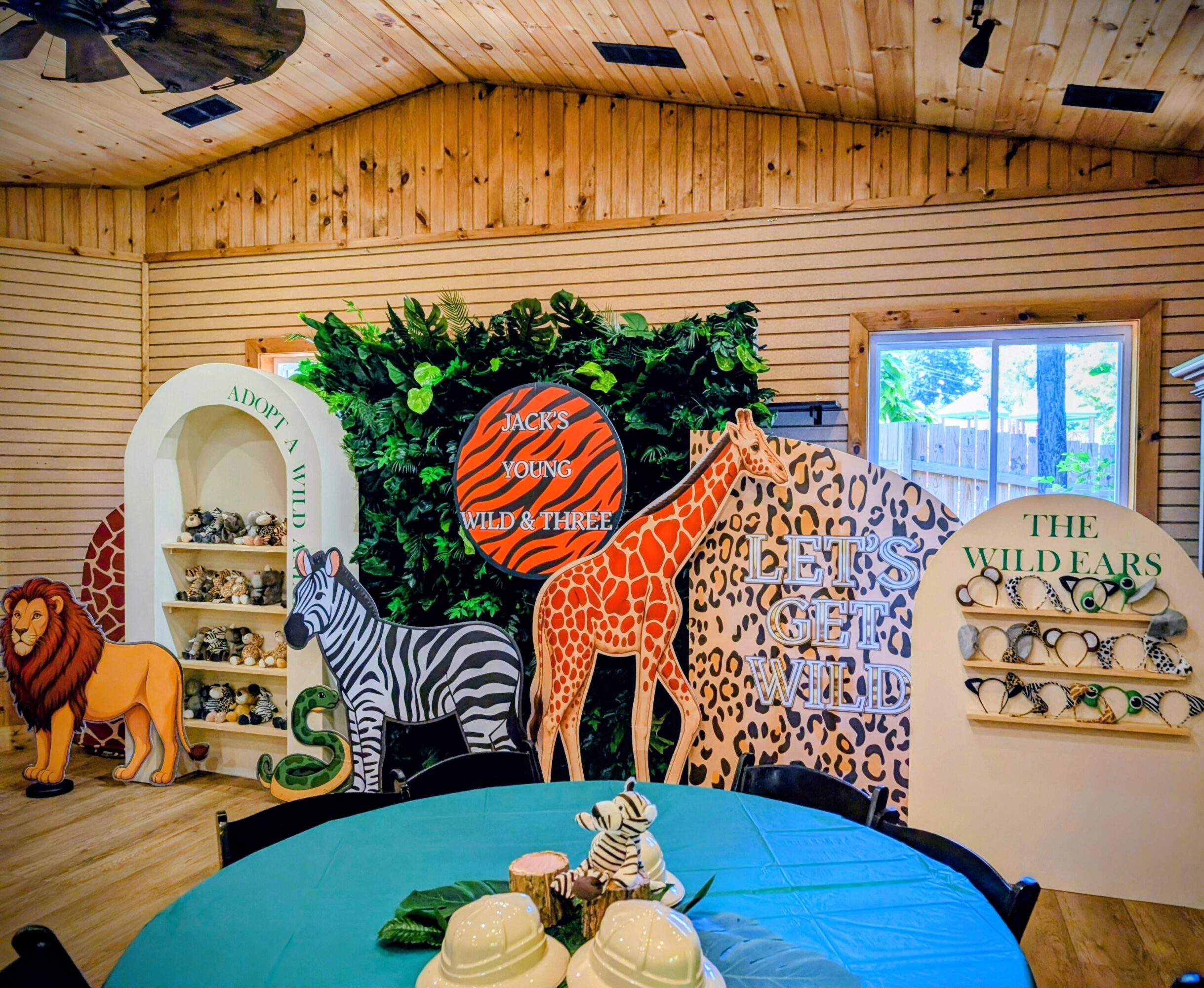 Indoor jungle-themed room with animal decorations, a round orange sign, and shelves with animal figurines, wooden walls, and a window.