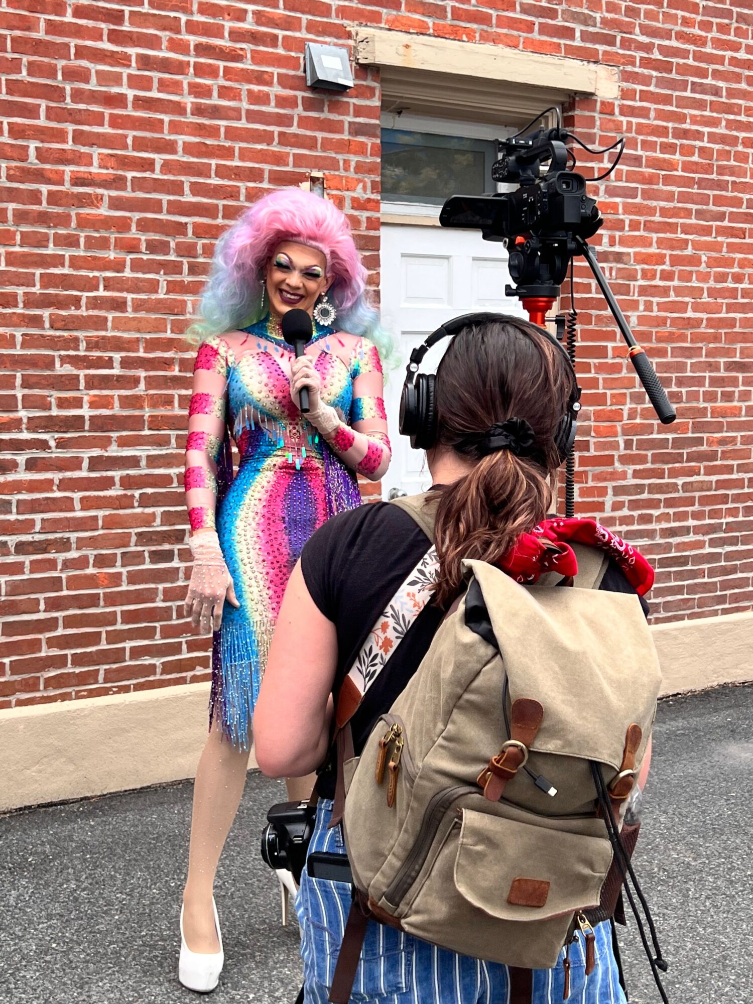 Two women, one in colorful sweater, the other with a backpack, standing outside near a brick wall and sidewalk.