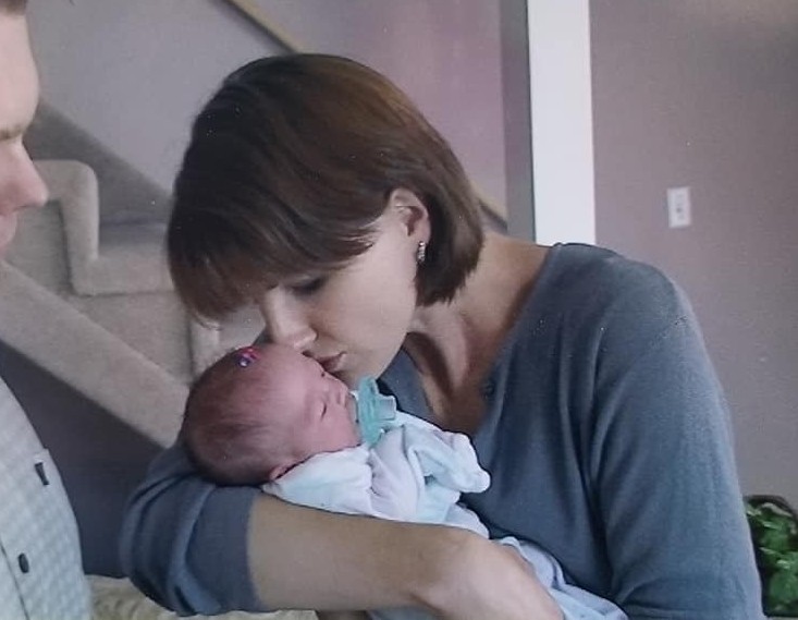 Woman holding a newborn baby close, indoors, with stairs in the background.