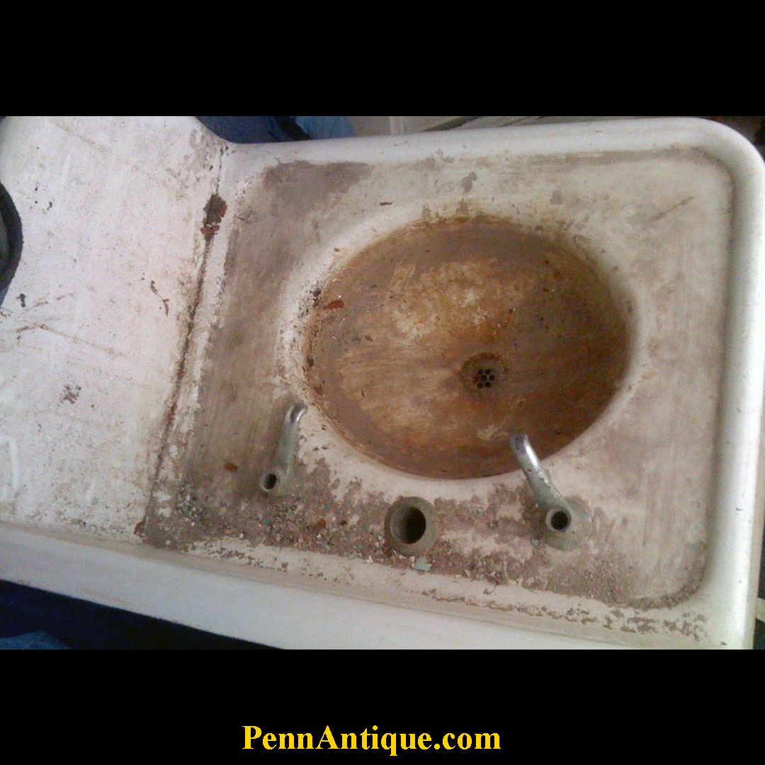 Rusty sink with stains and debris, two metal pipes, and a drain hole, in a dirty white basin.