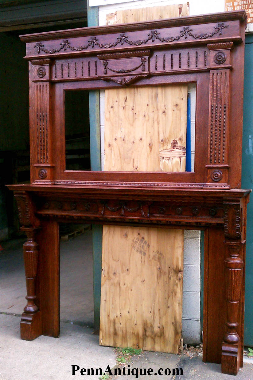 Decorative wooden fireplace mantel with carved details and columns, placed outdoors against a wooden and metal background.