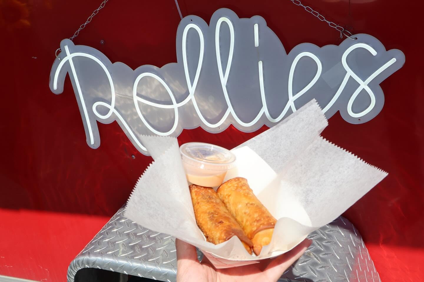 Two fried food items in a paper boat with dipping sauce, in front of a red background with a 'pallies' sign