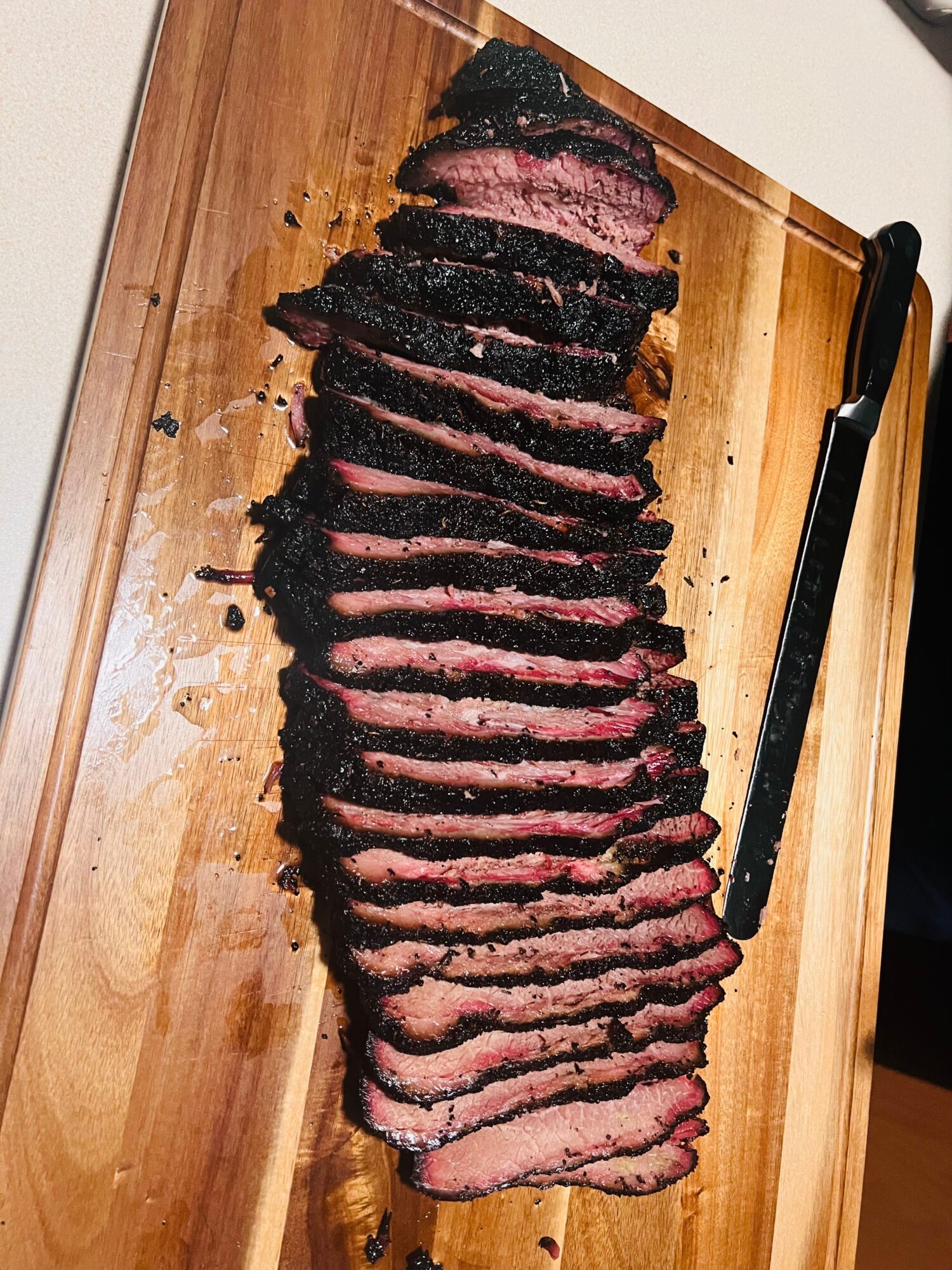 Sliced cooked steak on a wooden cutting board with a black-handled knife beside it.