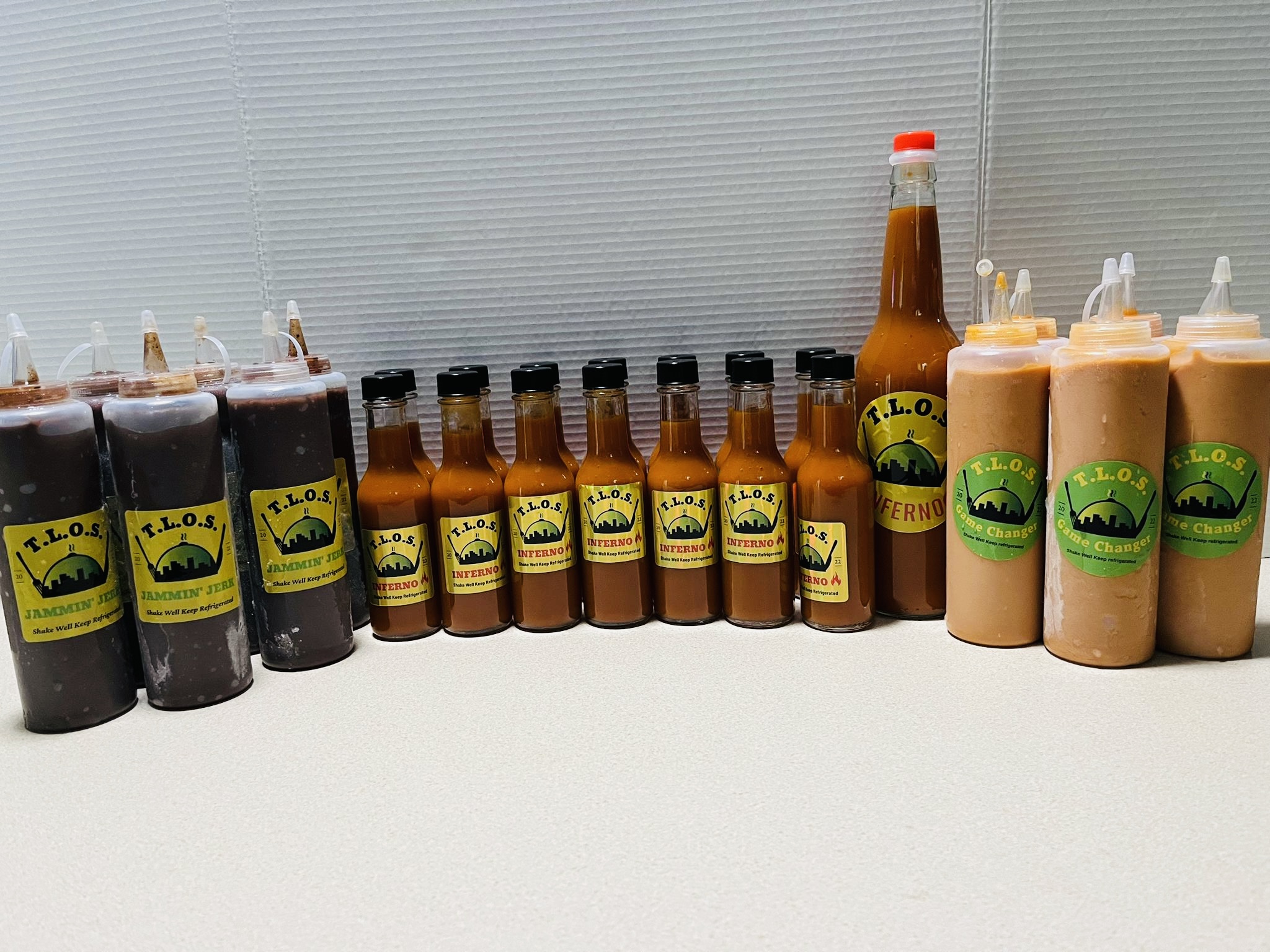 Row of bottles and squeeze bottles with yellow labels on a white surface, against a gray background.