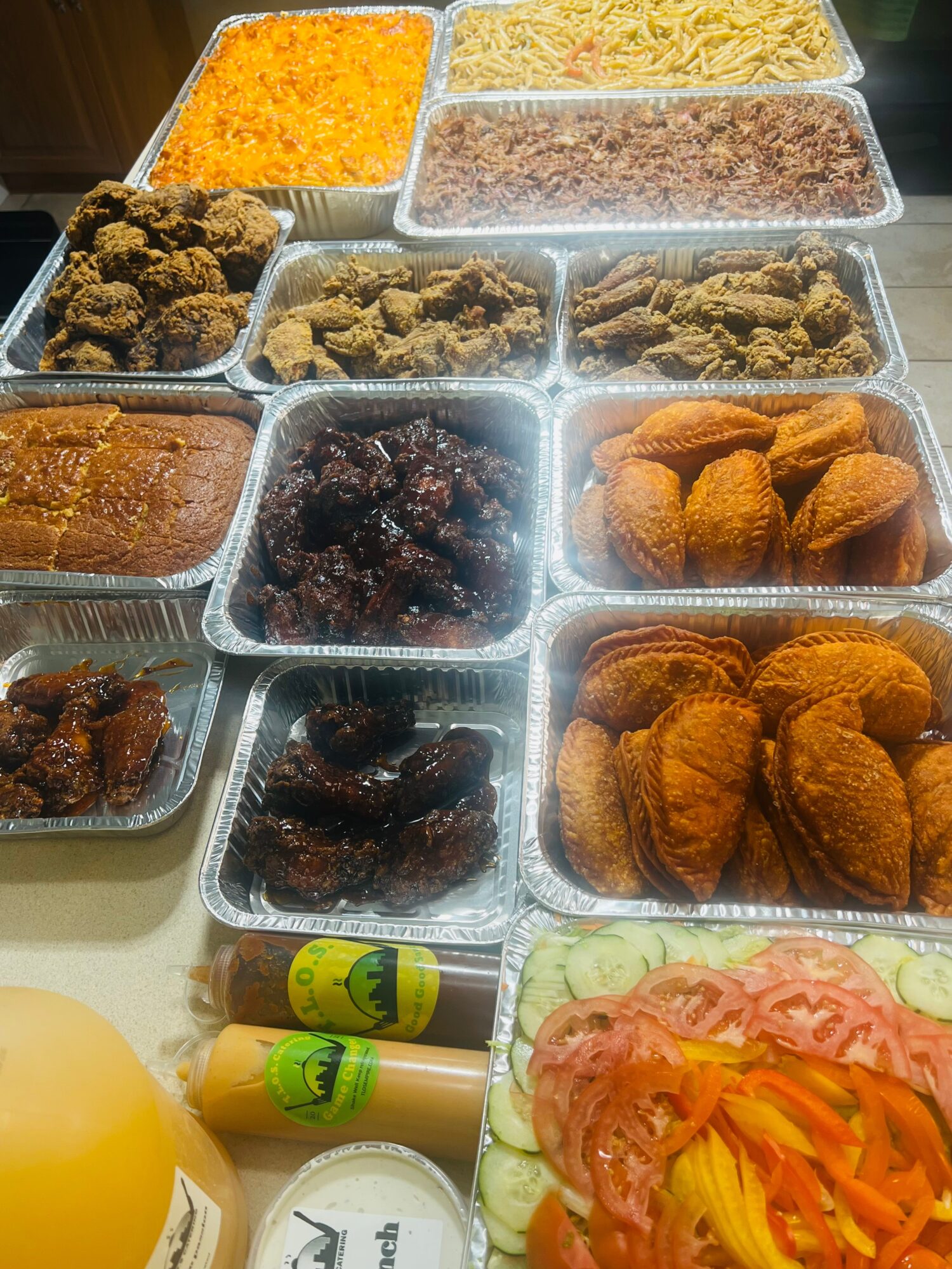 Assorted food containers with fried chicken, rice, beans, and vegetables, along with drinks and condiments on a table.