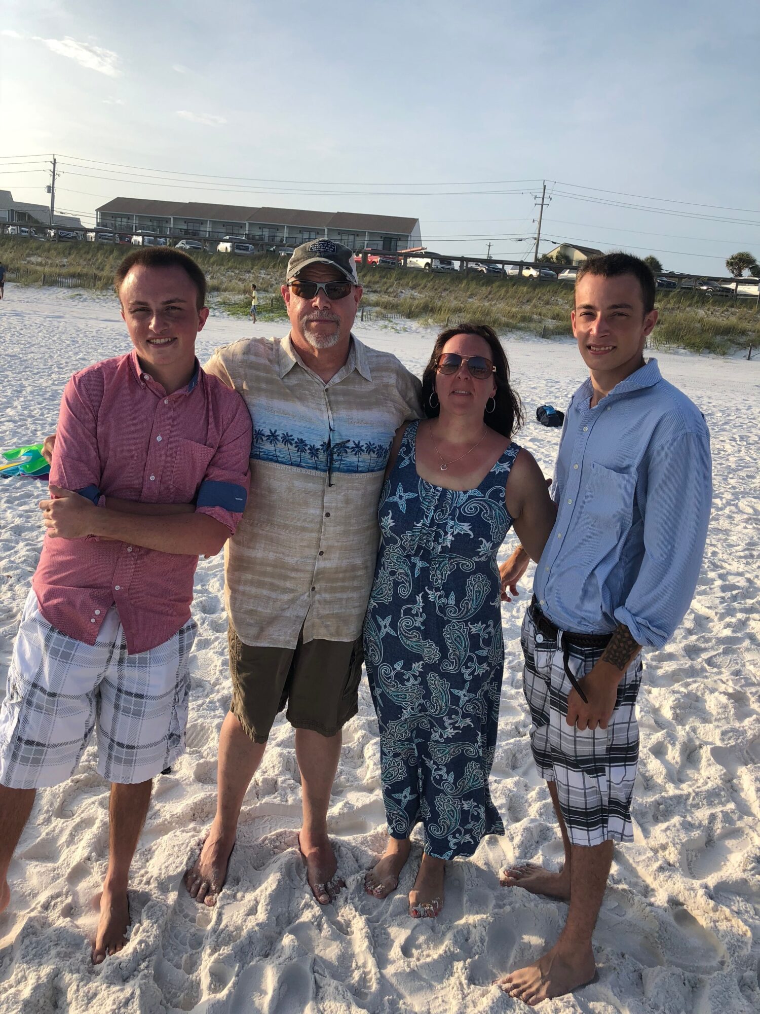 Three people standing on sandy beach, with water and a building in the background, under a clear sky.