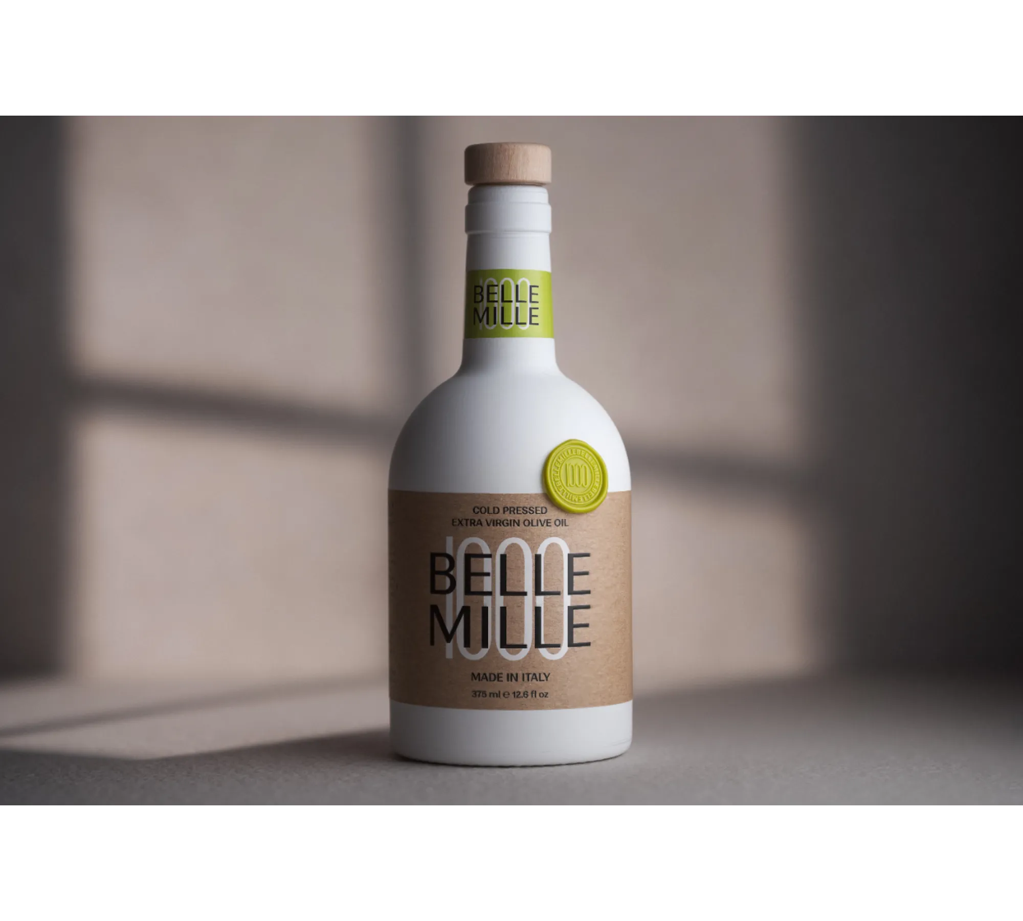 White bottle with beige and green label, standing on a surface with shadow, against a blurred background.