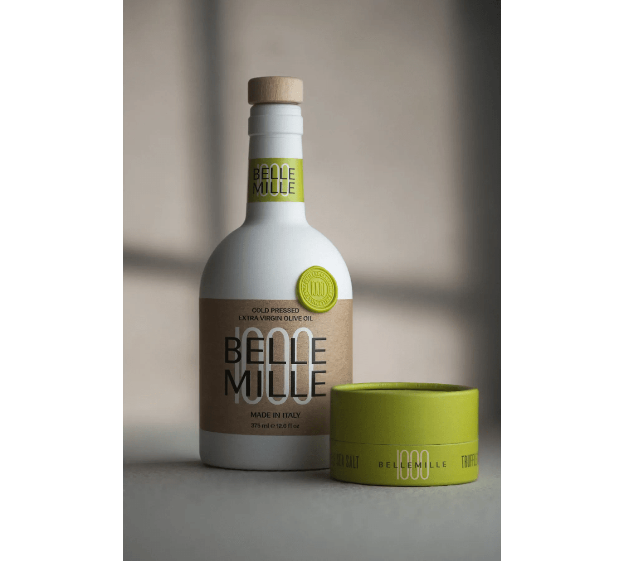 White bottle with beige label and green cap, next to a green container, on a gray surface.