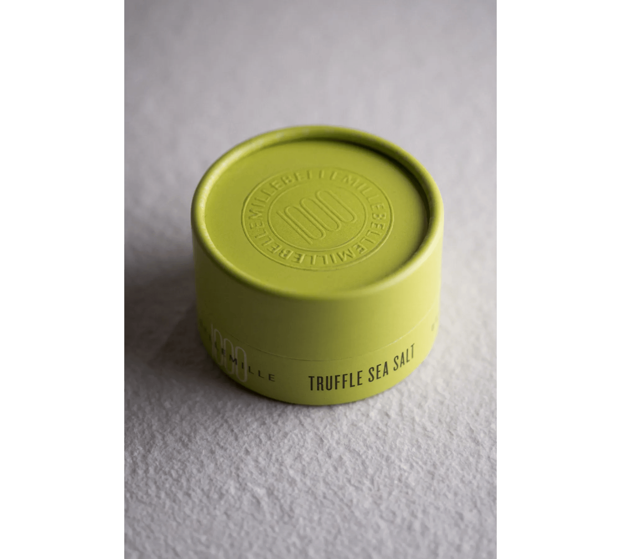Green container with embossed lid and label reading 'Truffle Sea Salt' on a textured surface.