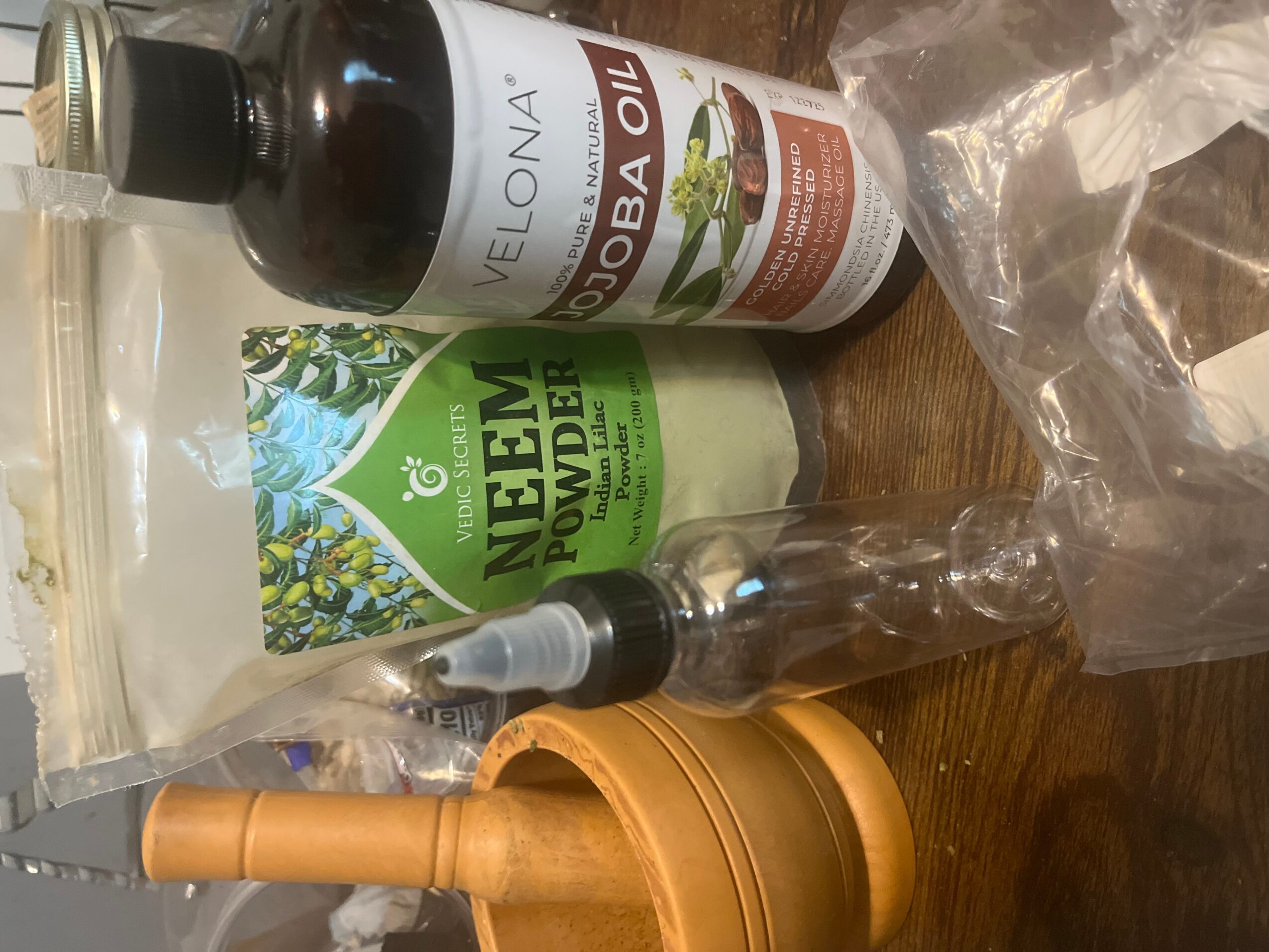 Bottles of neem oil and Velona neem water on a wooden surface, with a spray bottle and plastic bag nearby.