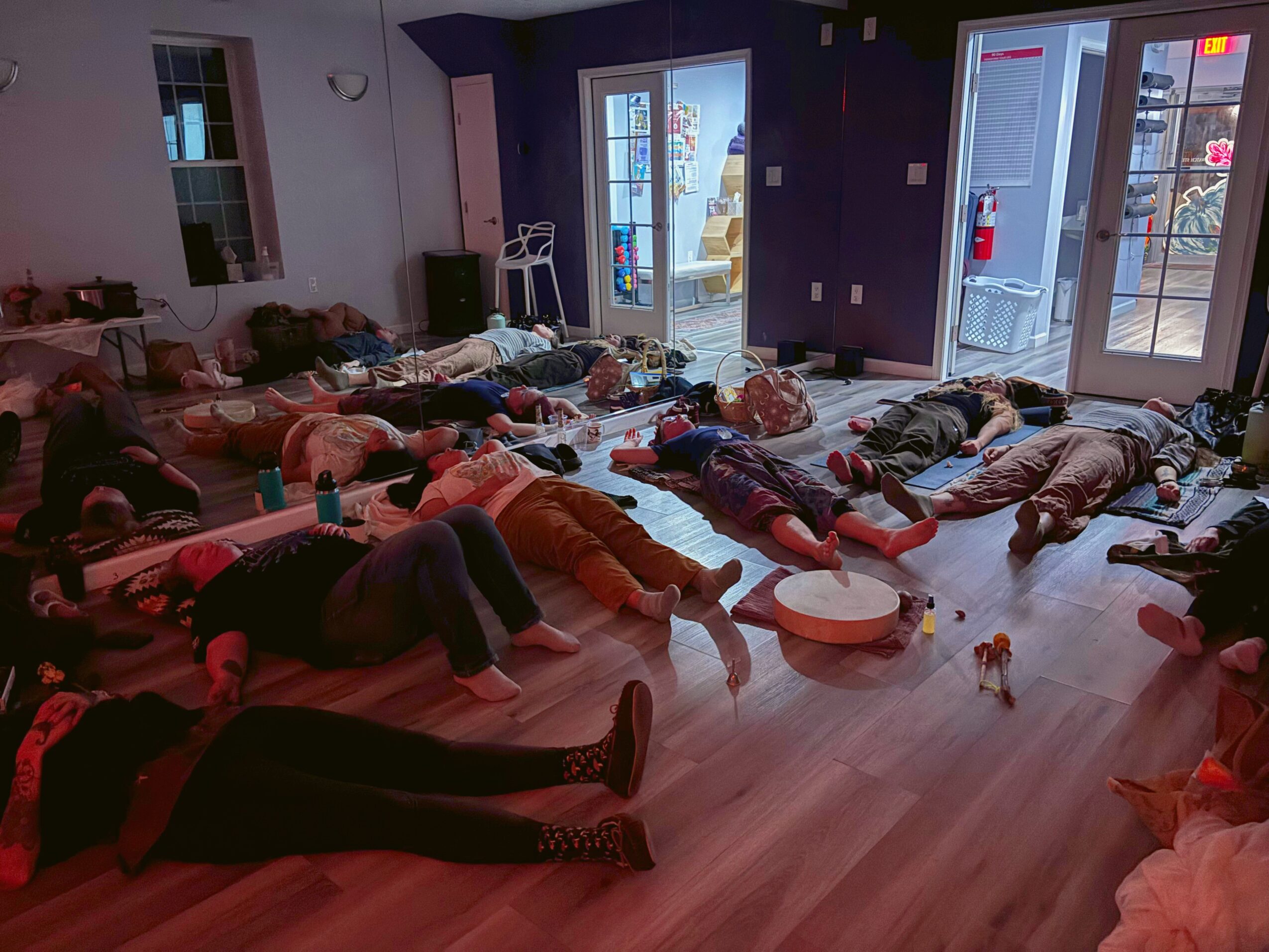 People lying on the floor in a room with large windows and a purple wall, some with objects nearby.