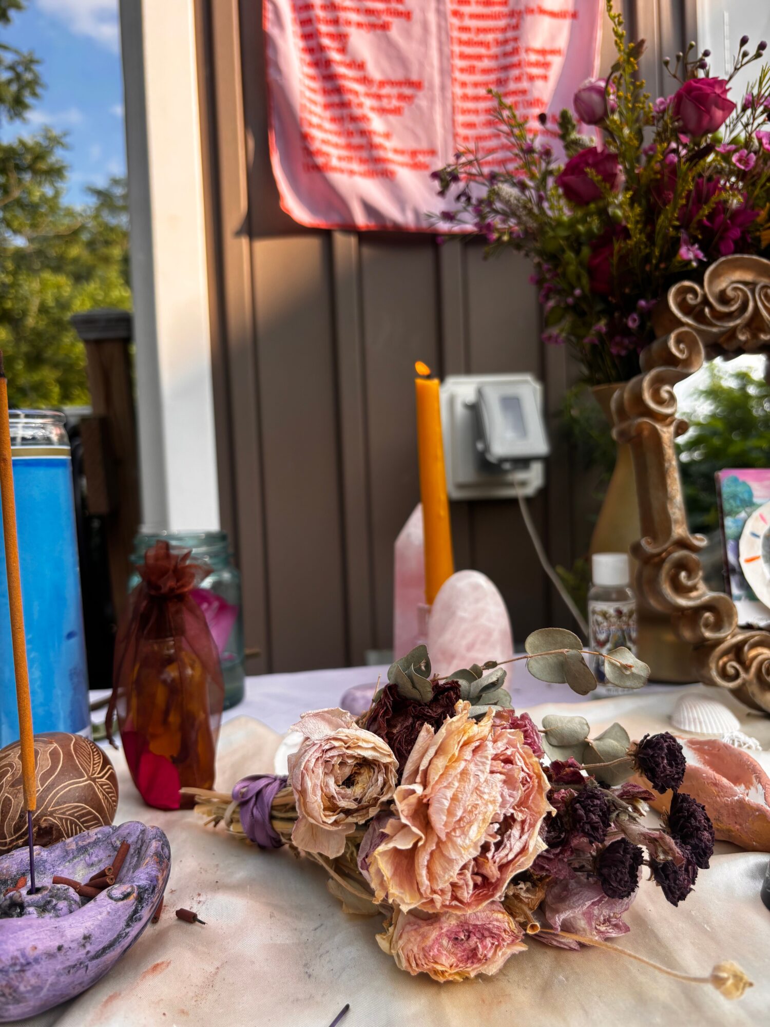 A table with flowers and desserts, with a background of a building and trees, viewed from the side.