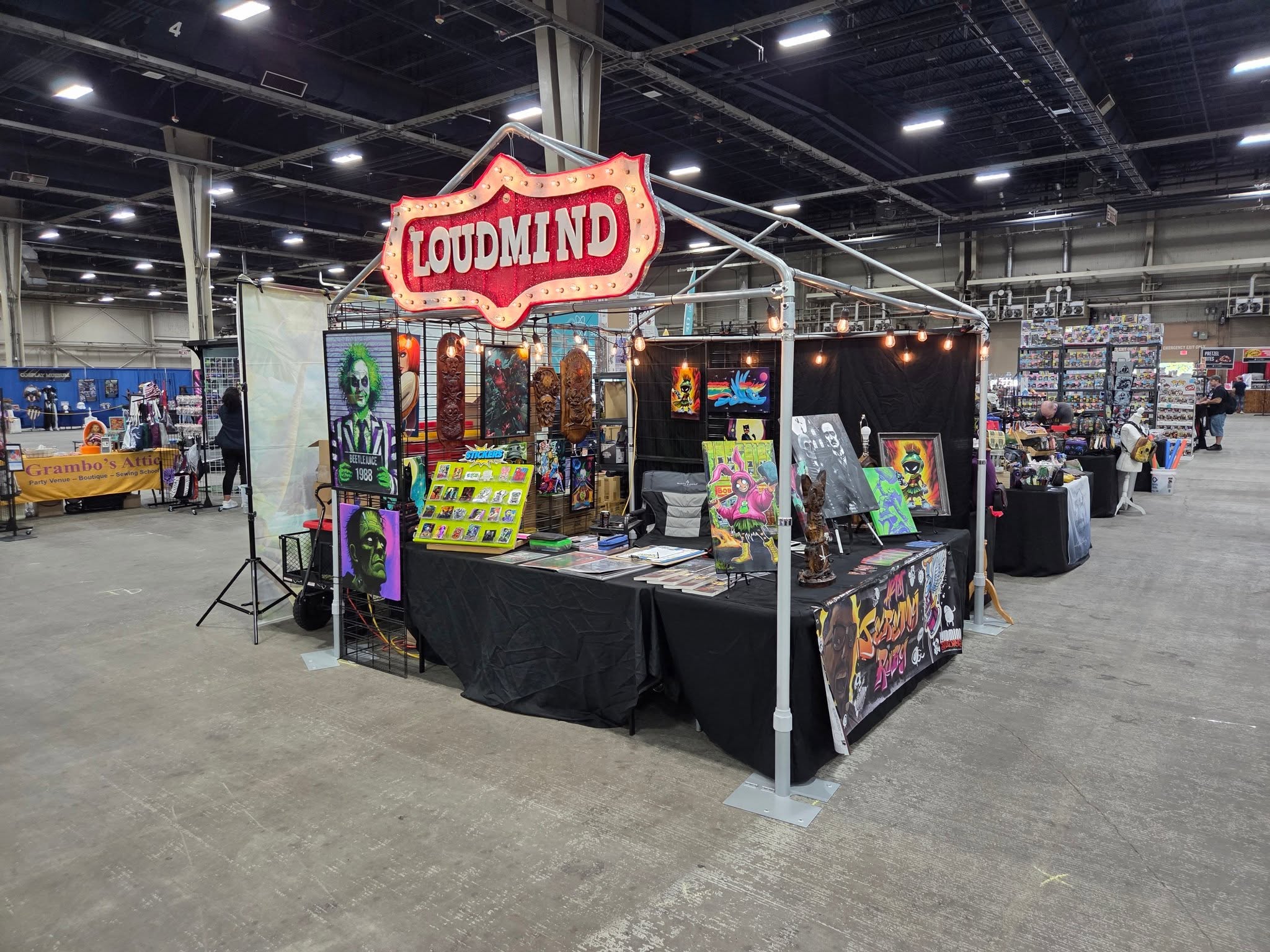 Art booth with colorful paintings and a sign reading 'LOUDMIND' inside a large indoor event space.