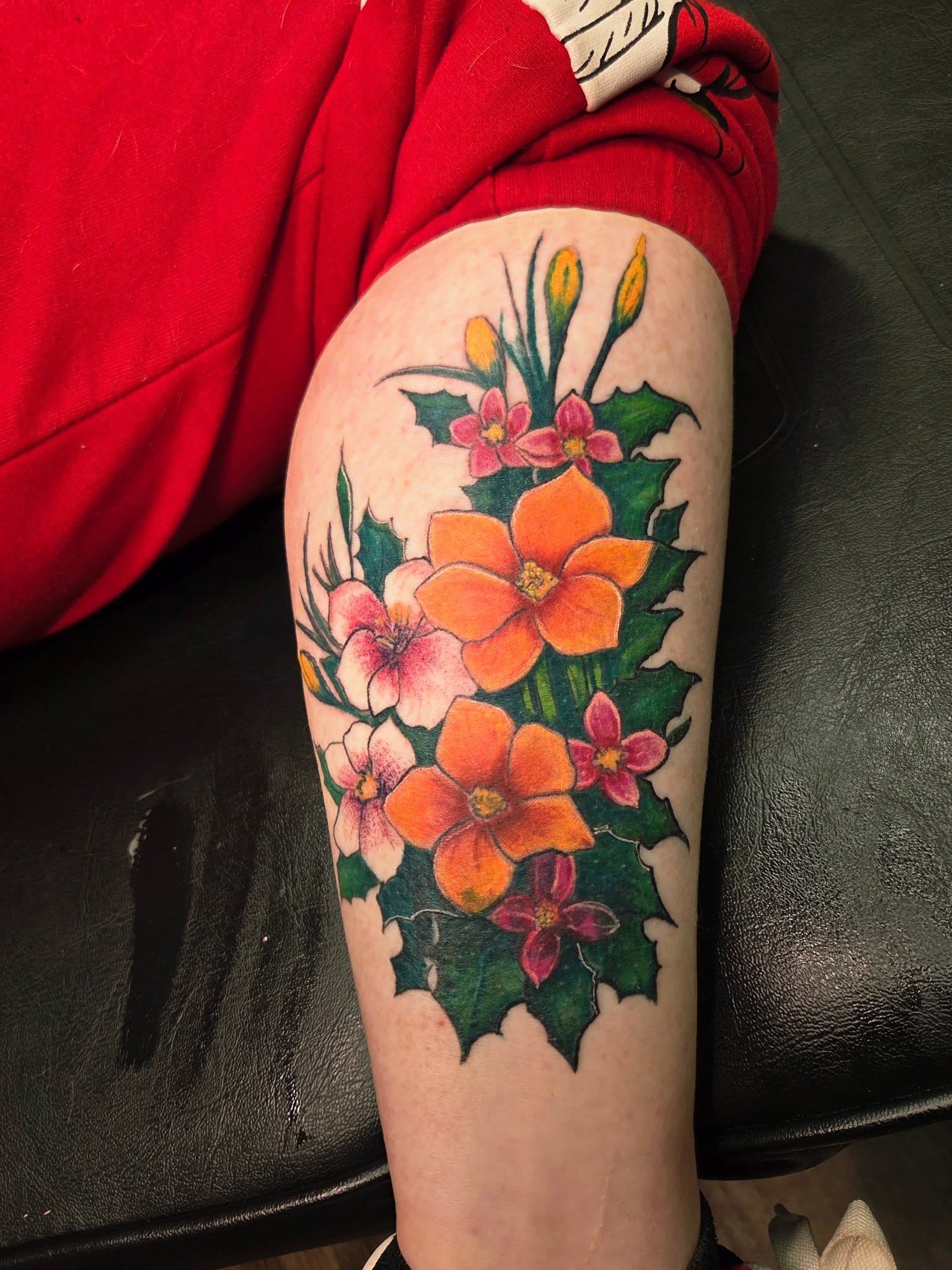 Colorful floral tattoo on person's arm featuring orange, pink, and purple flowers with green leaves.