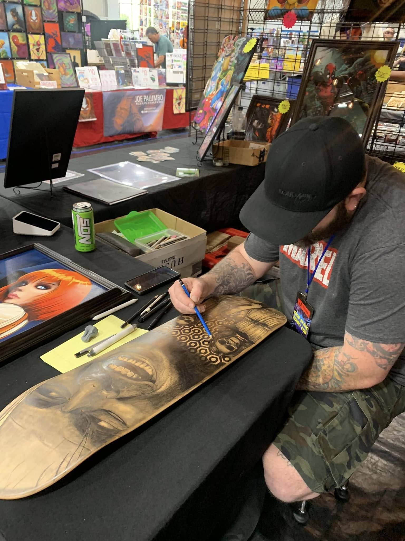 Person signing artwork at a table with comic books and art supplies, in a store or convention setting.