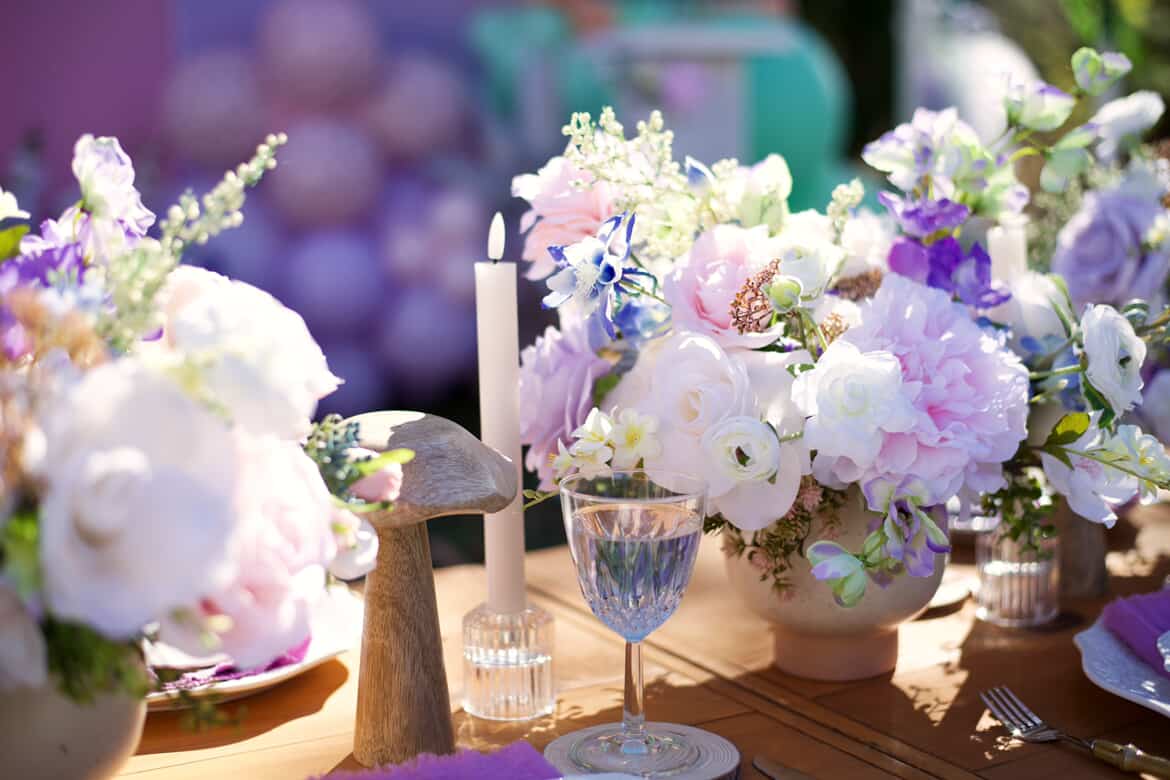Table setting with flowers, a candle, and glassware, decorated with pastel-colored flowers and greenery.