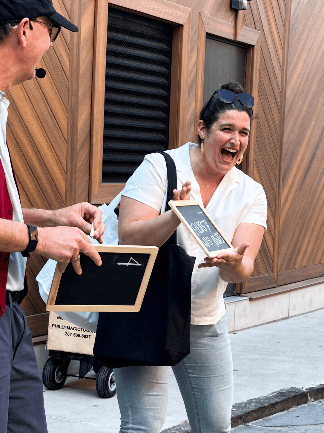 Woman laughing and holding a tablet, standing outside with wooden wall background.