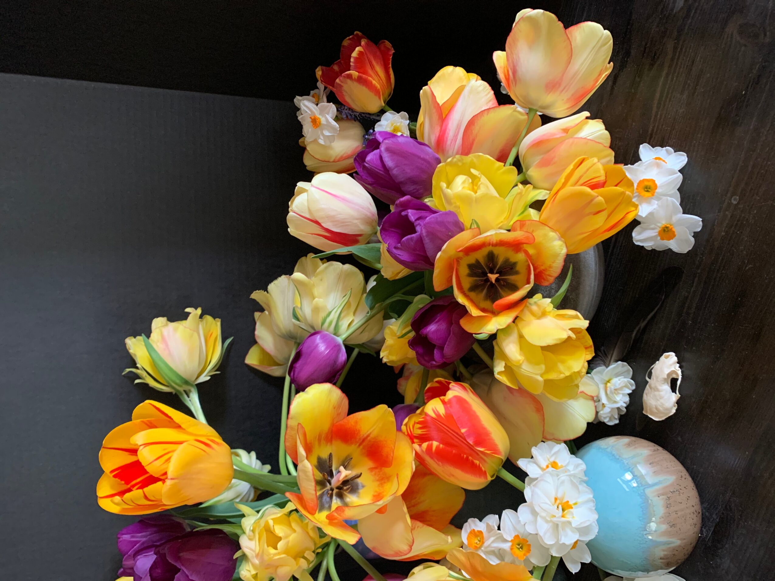 Colorful bouquet of tulips and small white flowers in a vase on a dark surface.