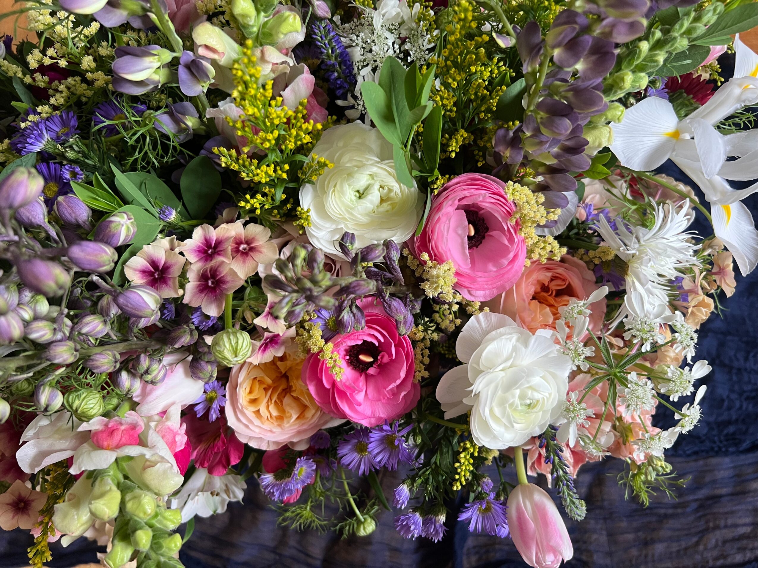 A colorful bouquet of various flowers including pink, white, purple, and yellow blooms with green foliage.