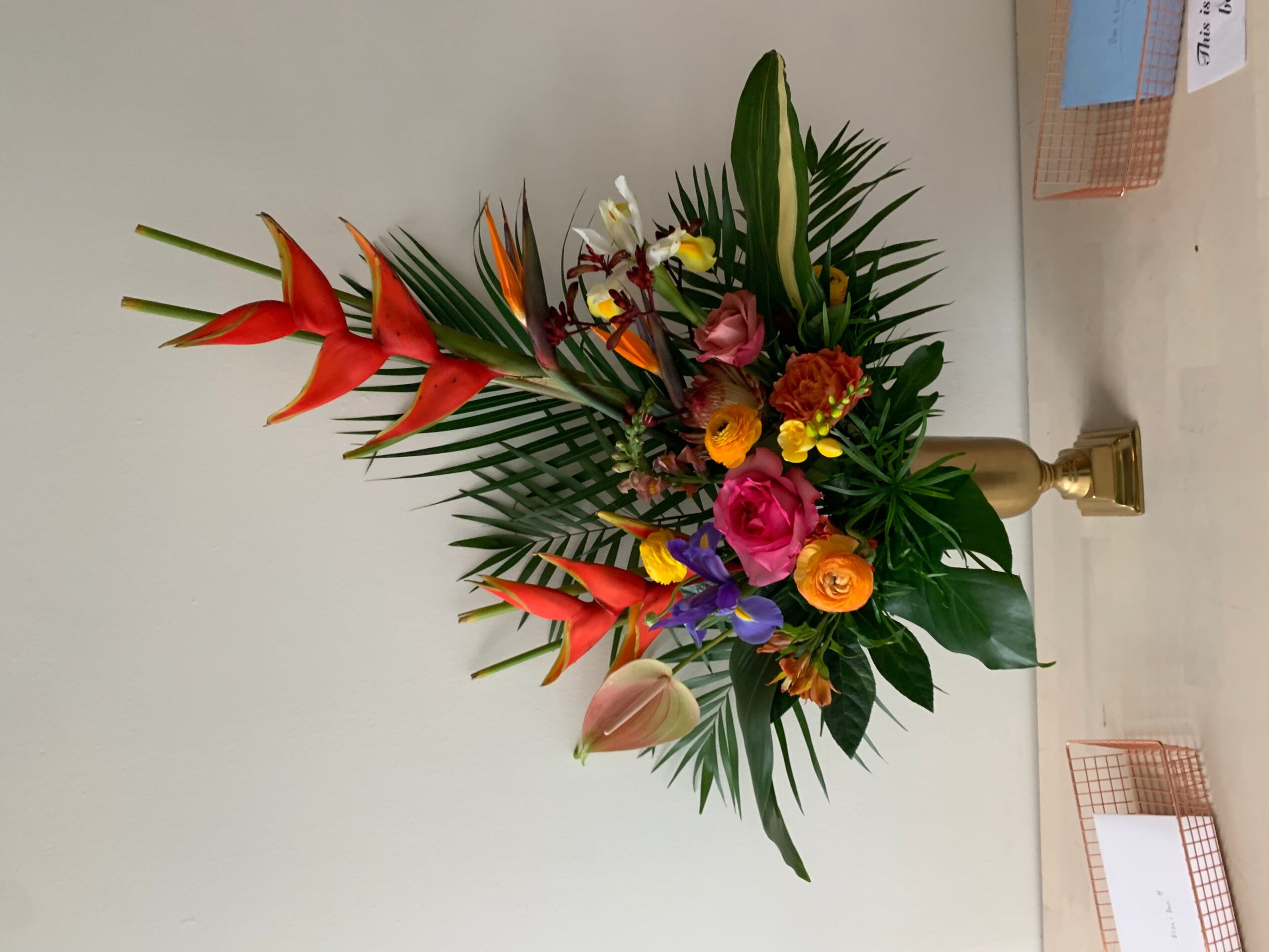 Colorful flower arrangement with pink, orange, purple, and yellow flowers, and green leaves, on a white surface.