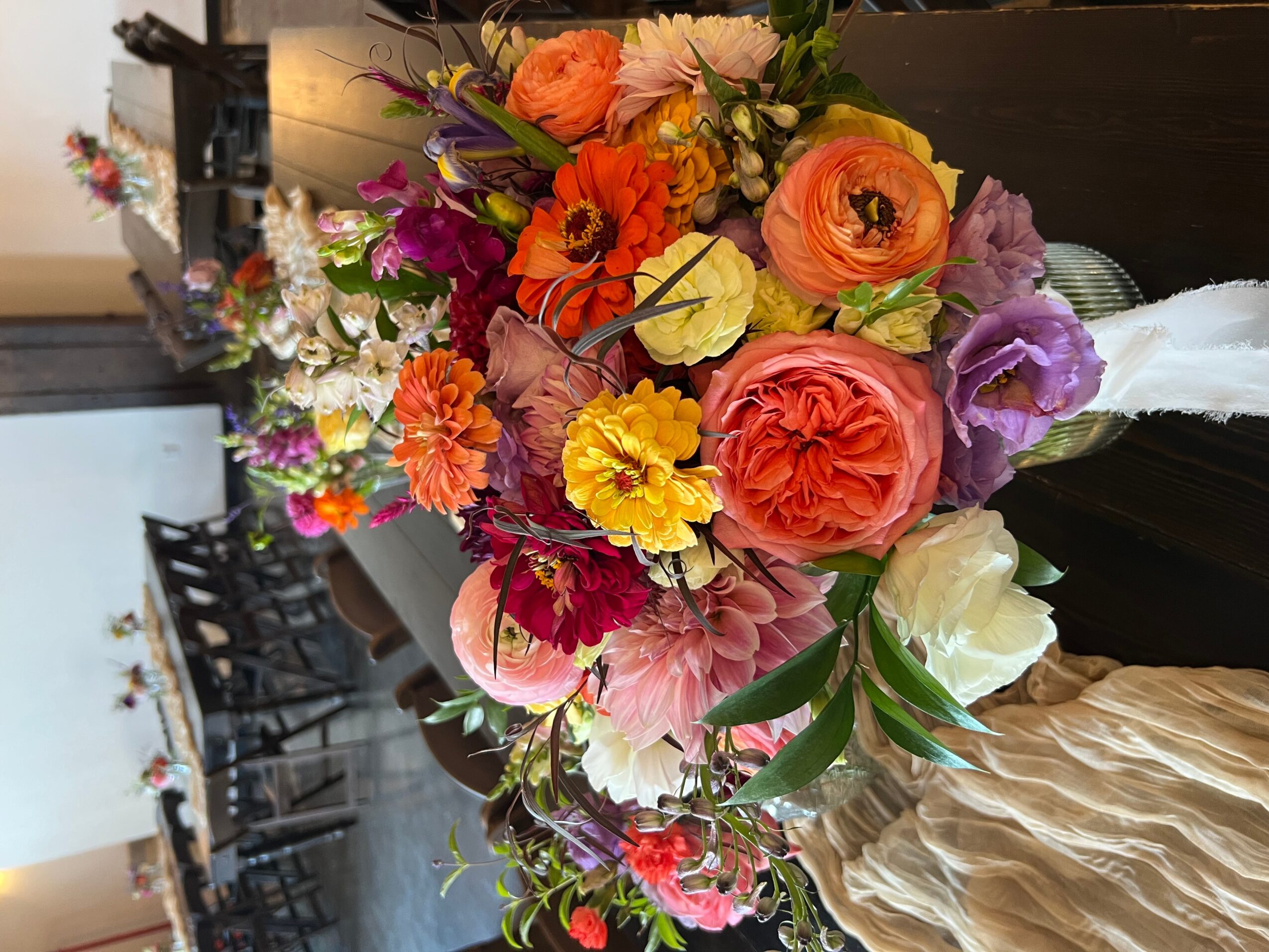 Colorful bouquet of various flowers including roses, peonies, and daisies on a dark table, with a blurred background.