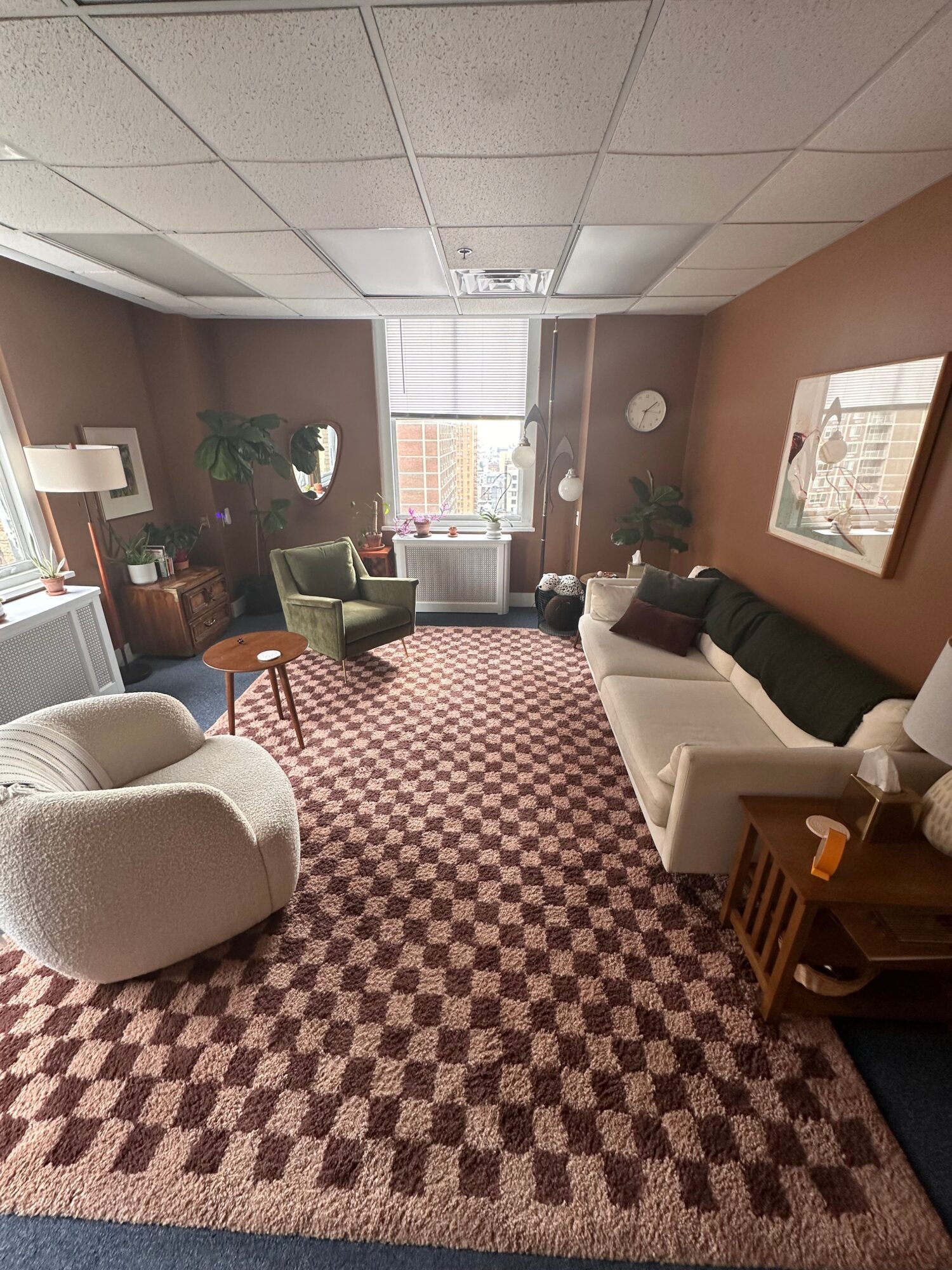 Living room with patterned carpet, armchair, sofa, window, and various furniture and plants.