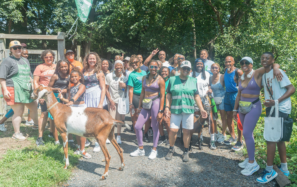Group of people outdoors, some smiling and waving, with a dog in front, trees in background.