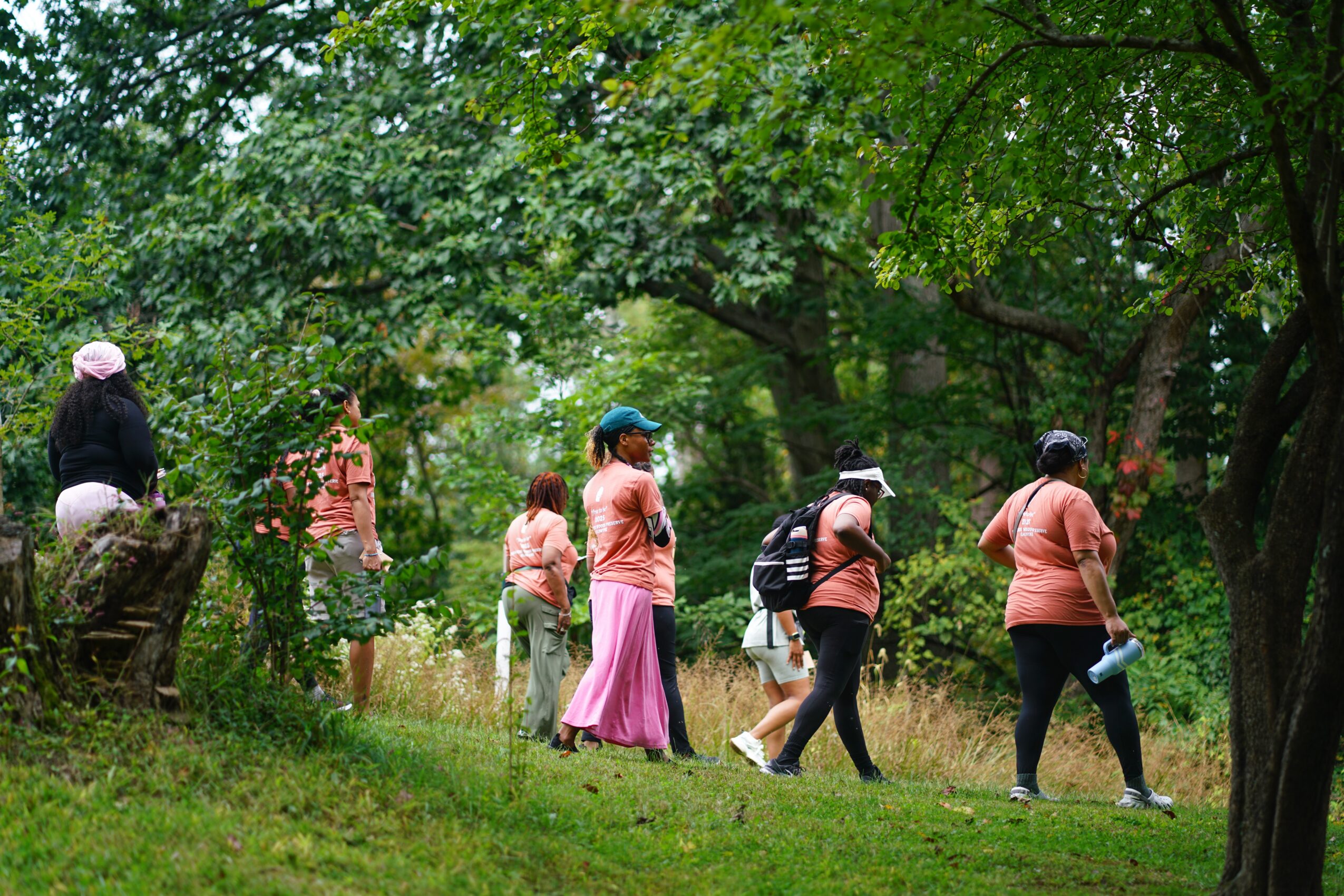Group of people walking along a path in a lush, green park with trees and grass.