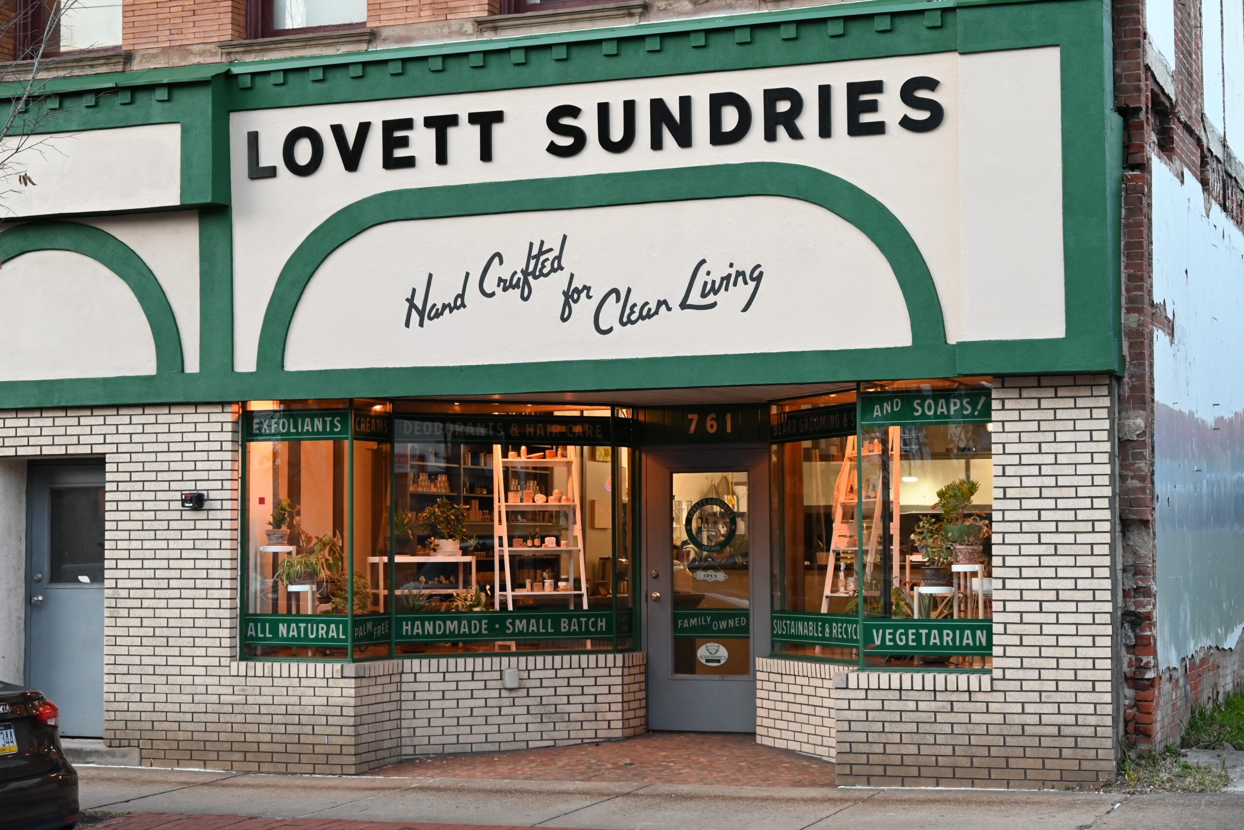 Storefront with sign reading 'Lovett Sundries' and large windows displaying products, brick exterior, and a door in the center.