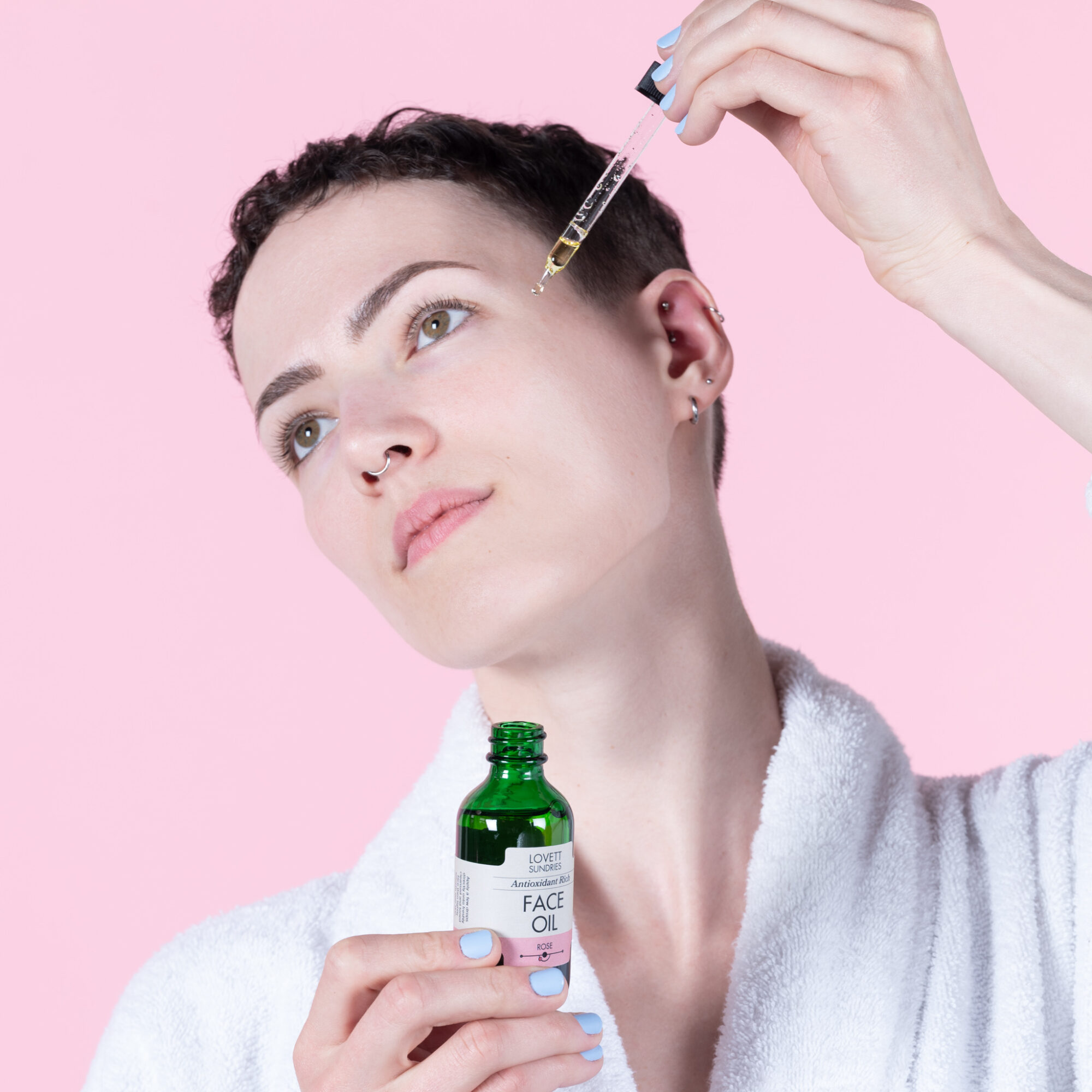 Person with short hair receiving facial injection from a healthcare professional, holding a small bottle, against a pink background.