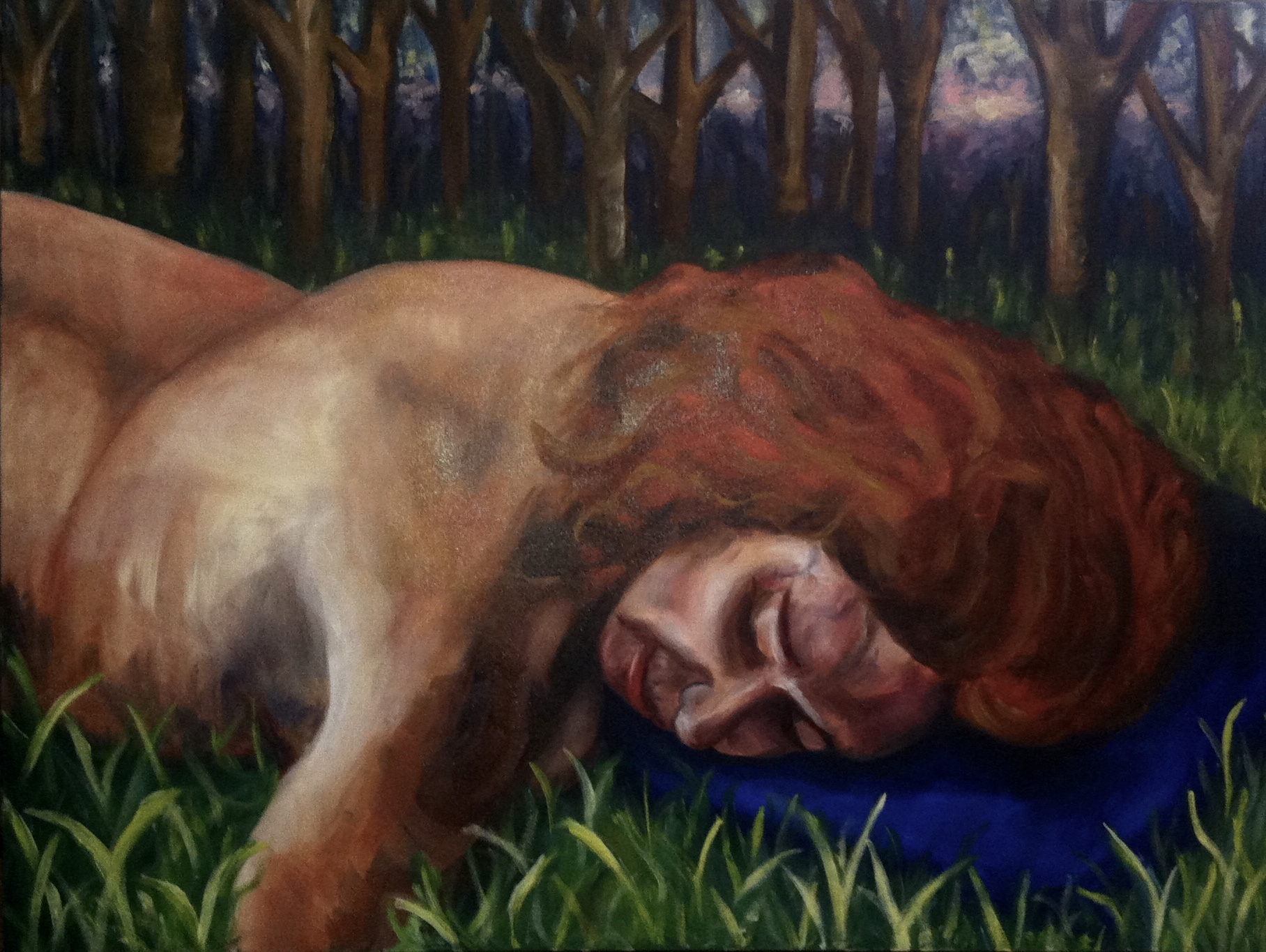A woman with red hair lies on her side on grass, eyes closed, in a forest setting.