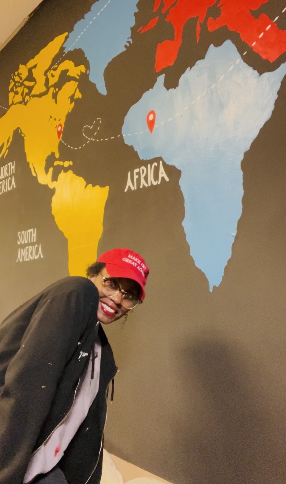 Person wearing a red cap and glasses smiling in front of a world map showing Africa and other continents.