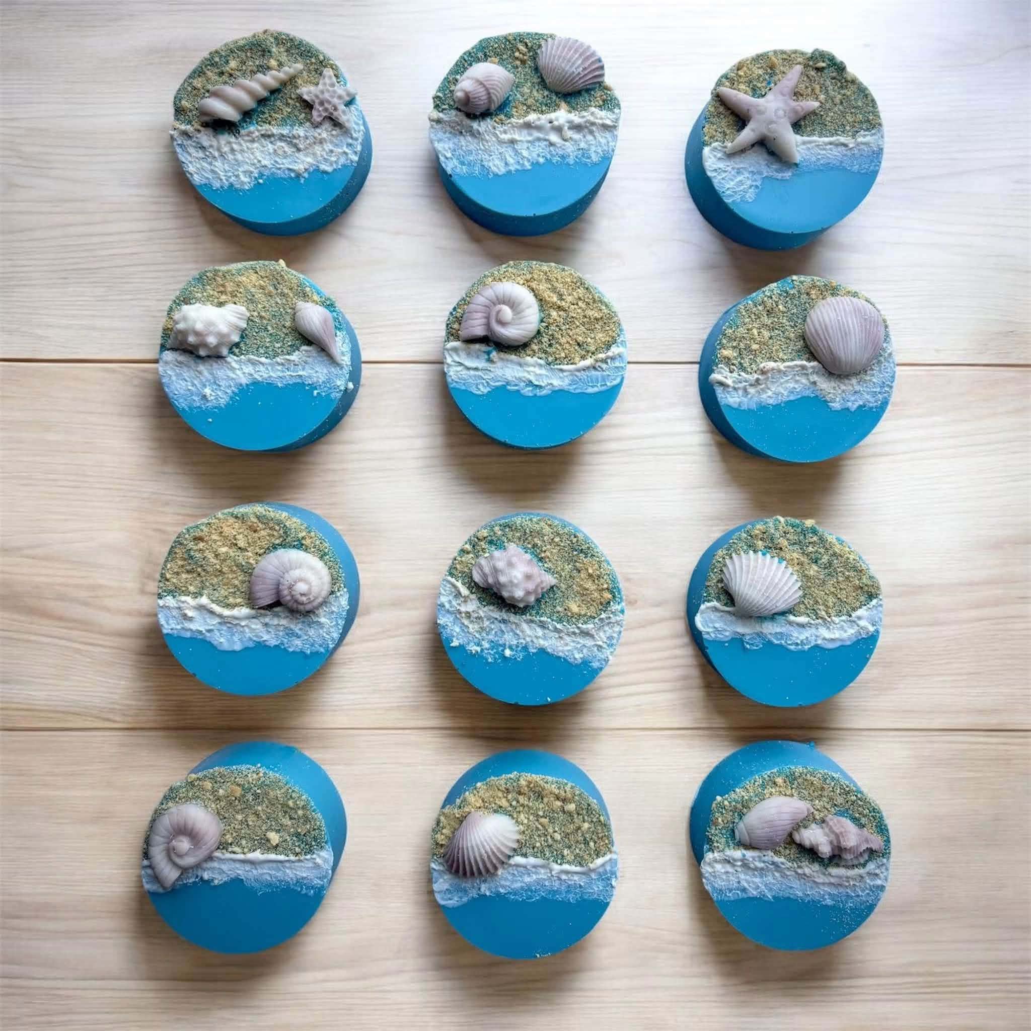 Collection of twelve seashell-themed cake toppers with sand and water details, arranged on a wooden surface.
