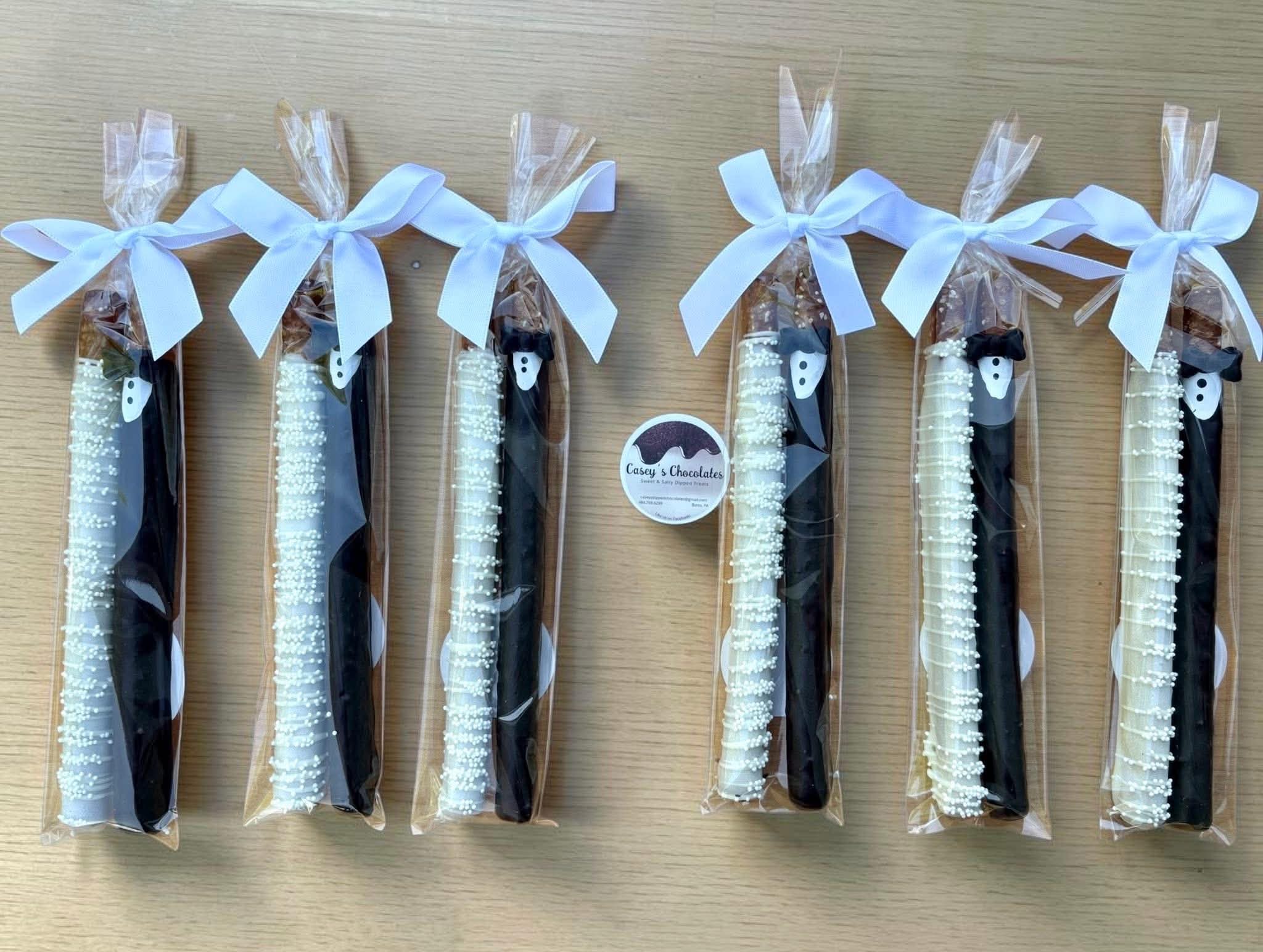 Six packaged items with white bows on top, arranged in a row on a wooden surface.