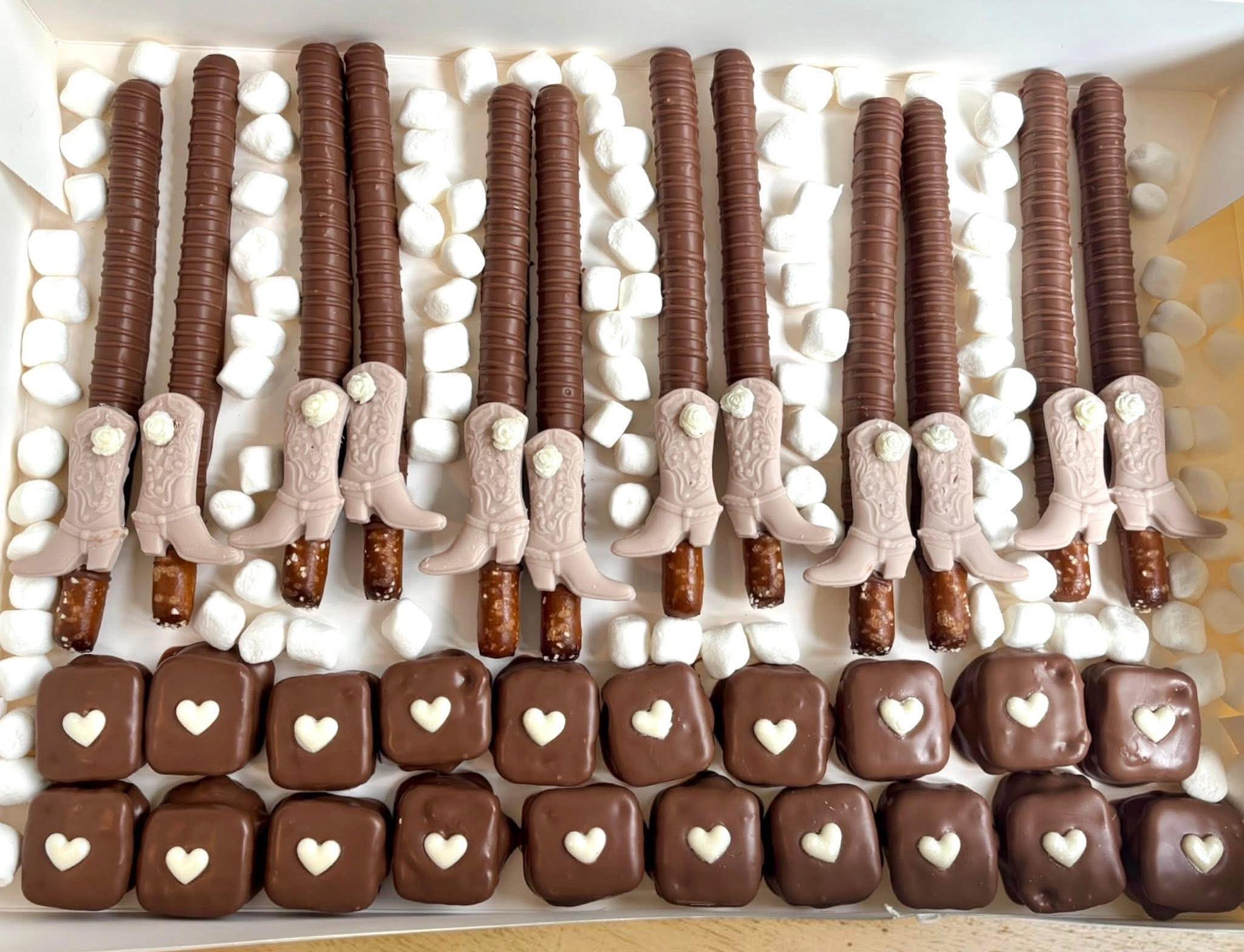 A tray of decorated chocolate treats with sticks, hearts, and white and brown toppings, arranged in rows.