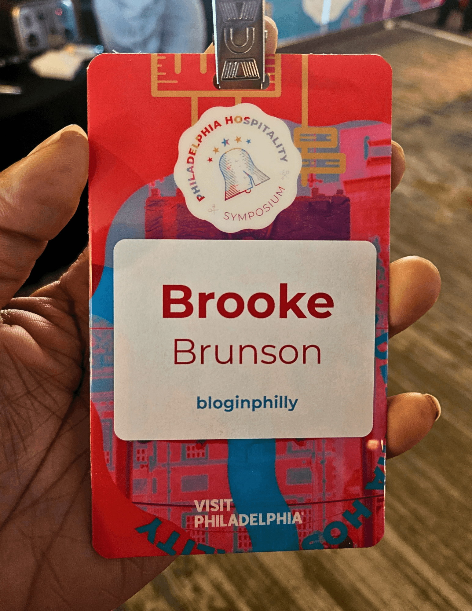 ID badge with name Brooke Brunson, logo of a hospital, and a colorful background, held in hand.