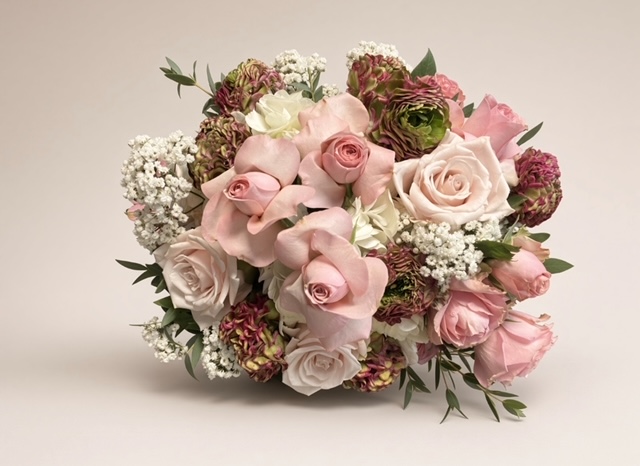 A bouquet of pink, white, and purple flowers with green leaves on a plain background.
