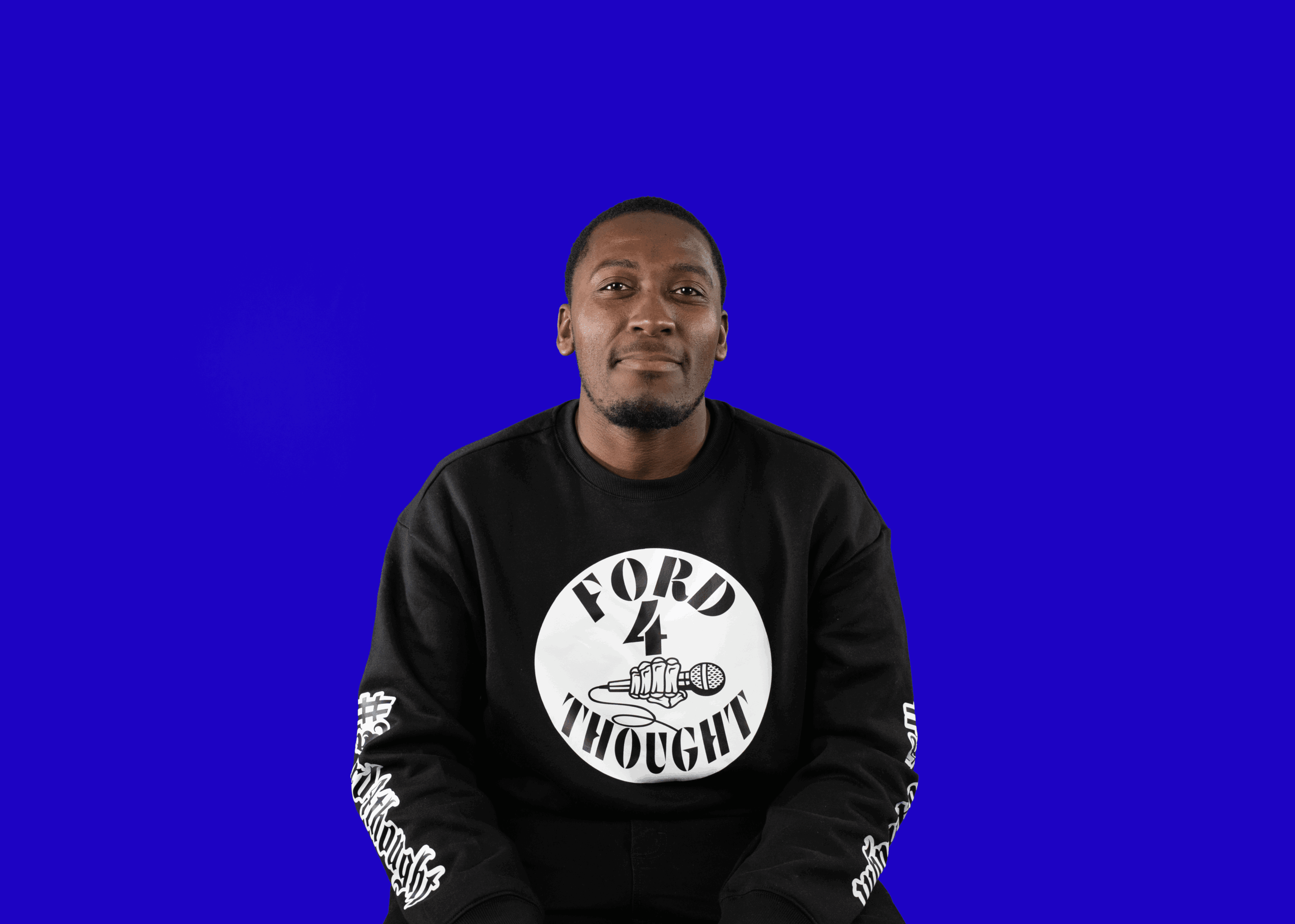Person with short hair wearing a black sweatshirt with white text and graphics, sitting against a blue background.