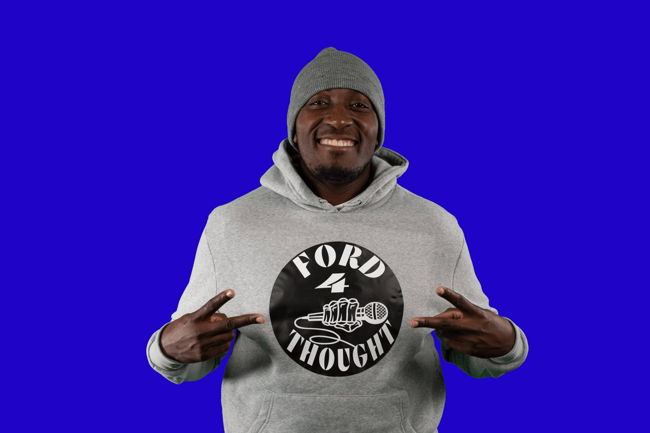 Smiling person wearing a gray hoodie and beanie, pointing at a logo on the chest, against a blue background.