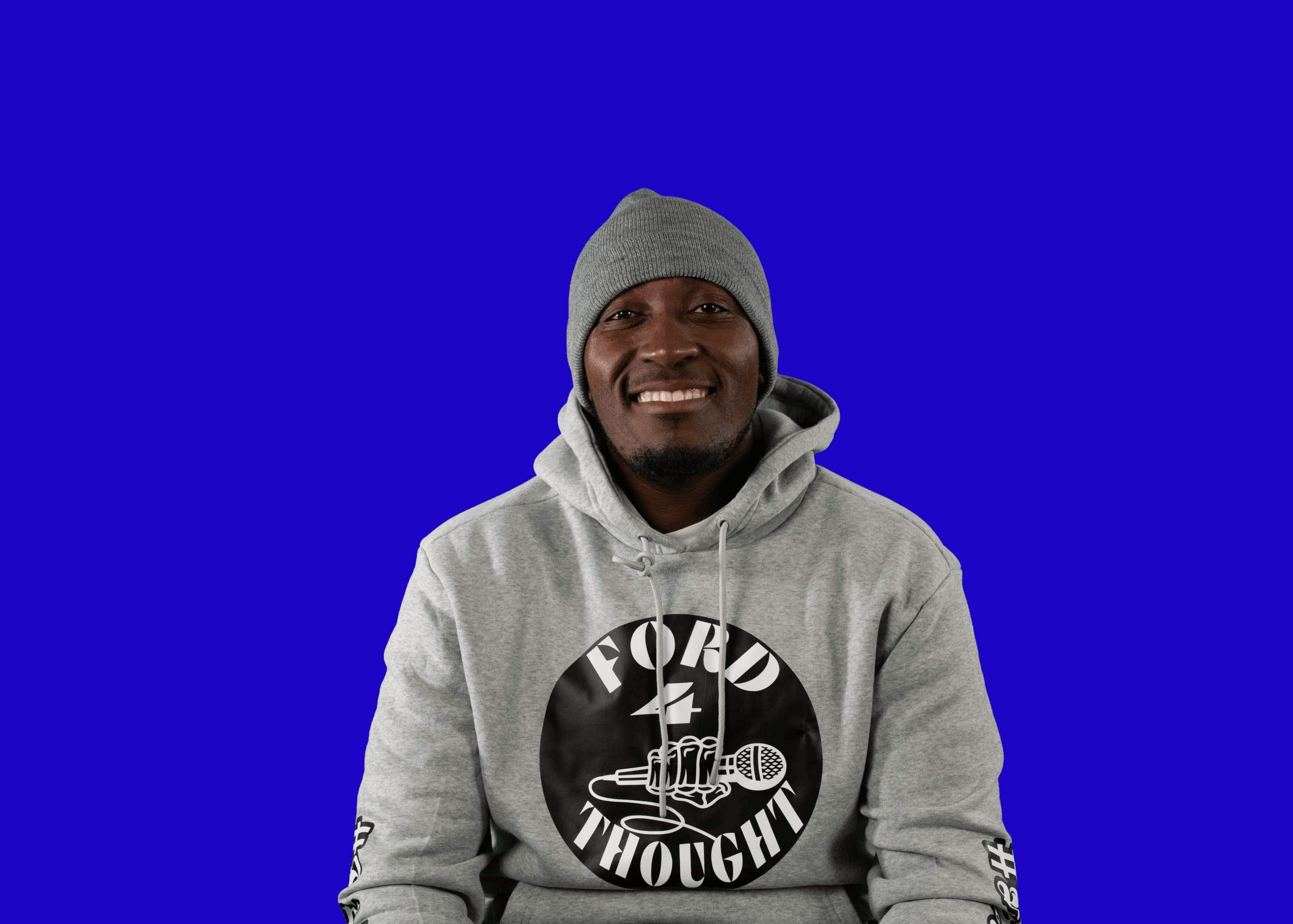 Smiling person wearing a gray hoodie and gray beanie against a blue background.