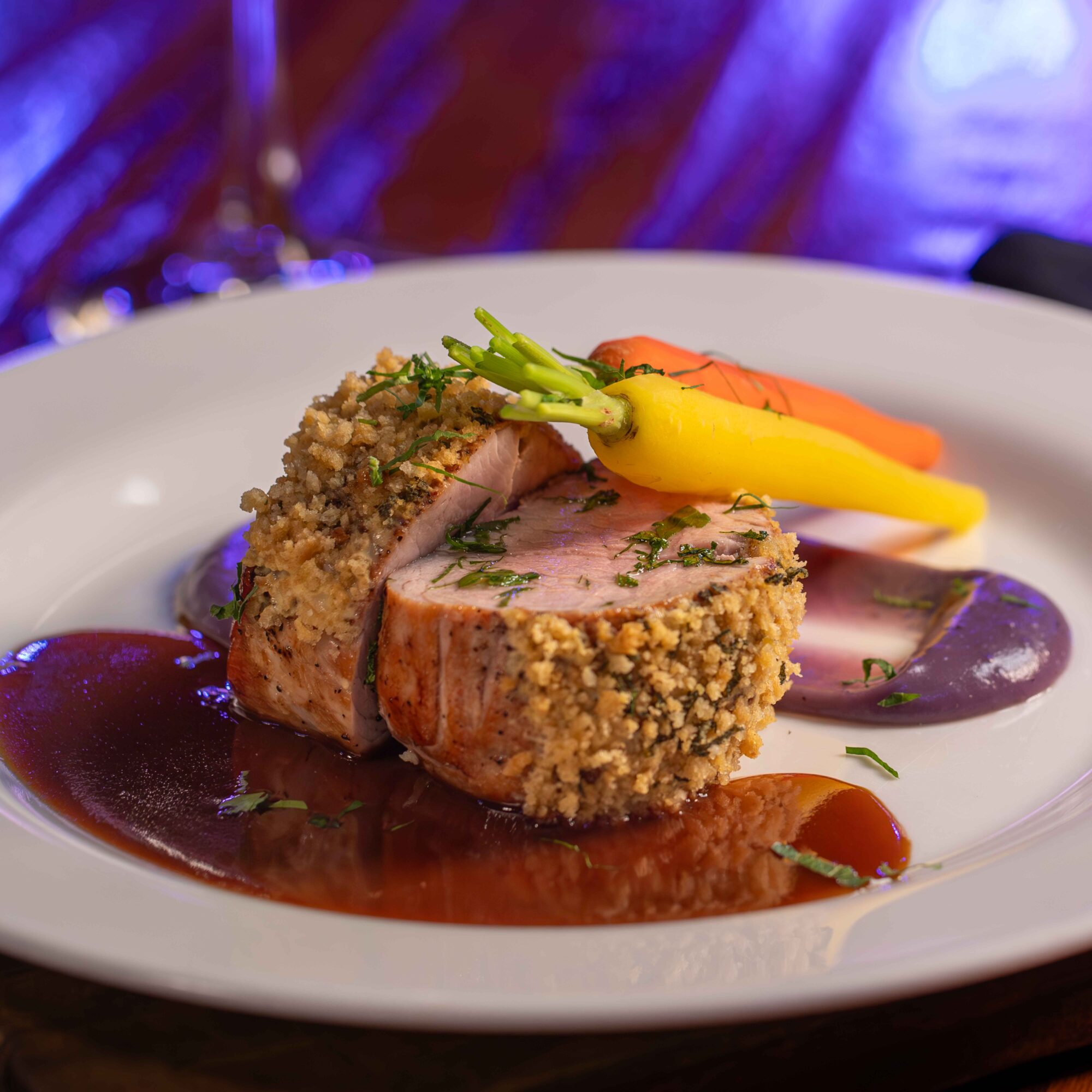 A plated dish with a breaded meat portion, colorful vegetables, and sauce, garnished with herbs on a white plate.